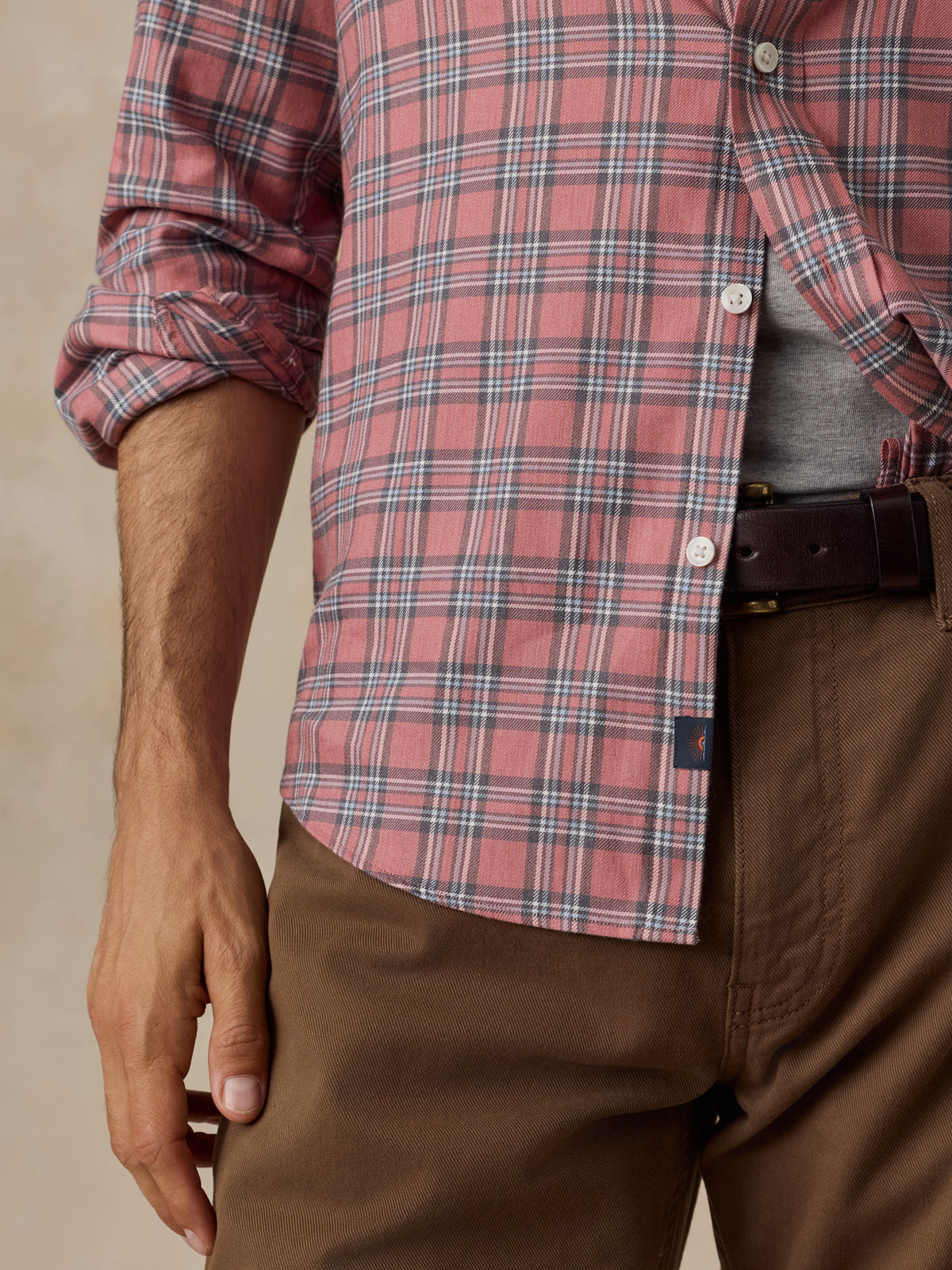 A close-up of a man wearing a red and blue plaid button-down shirt, brown pants, and a dark brown belt.