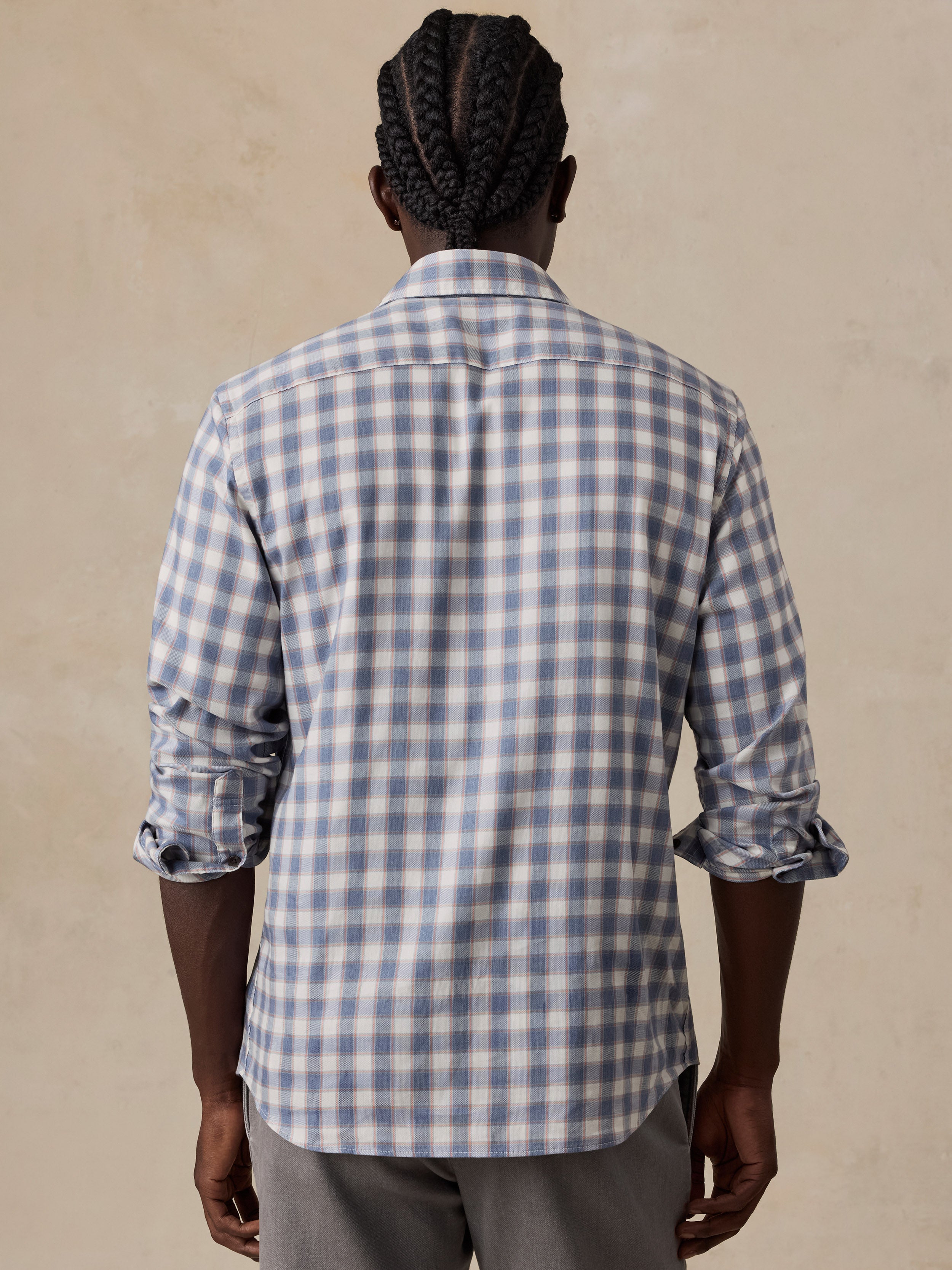 A man wearing a light blue and white gingham check long-sleeve button-down shirt, paired with gray trousers.