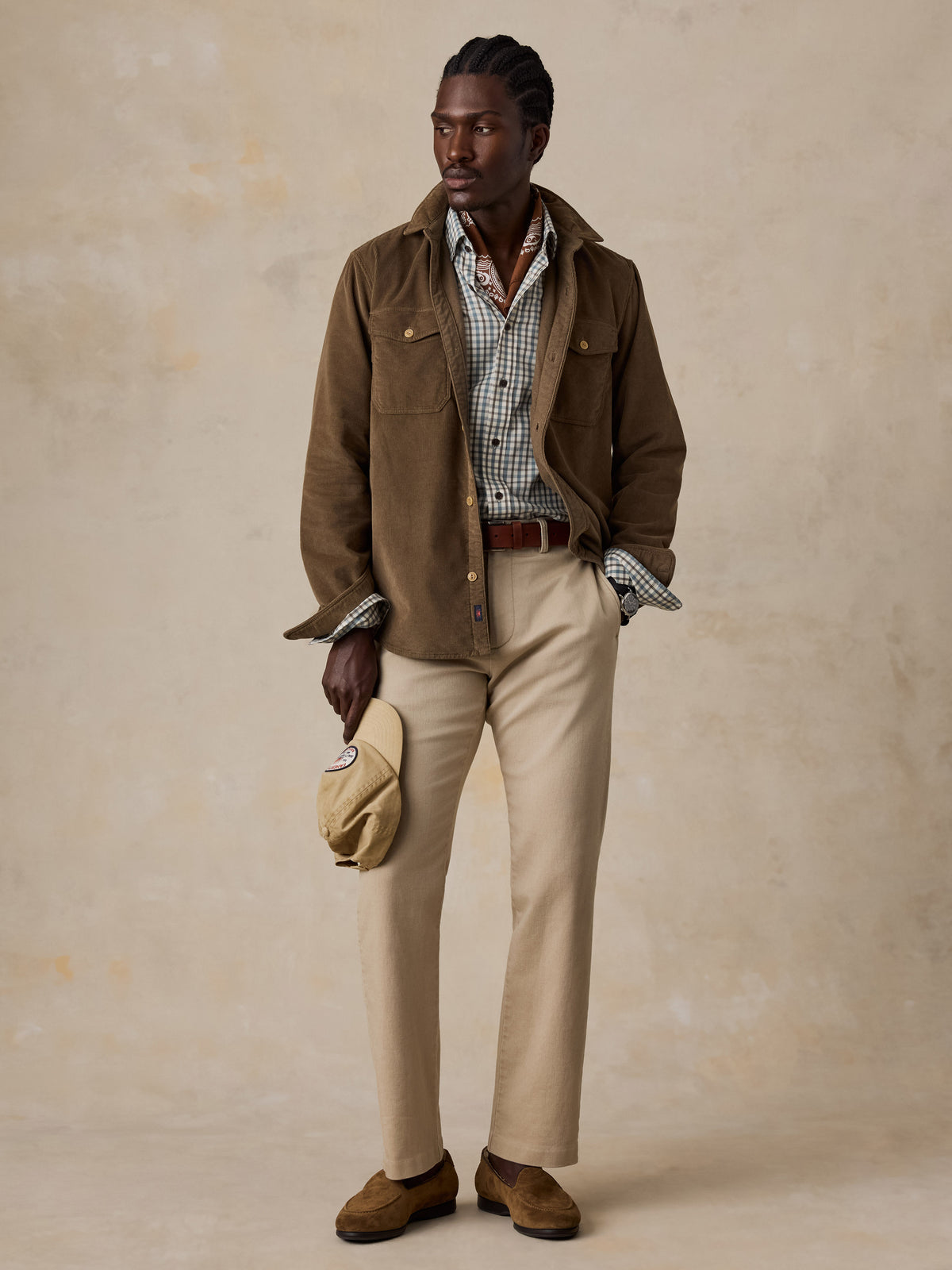 A man wearing a corduroy shirt over a plaid shirt and beige pants, image 2 of 5