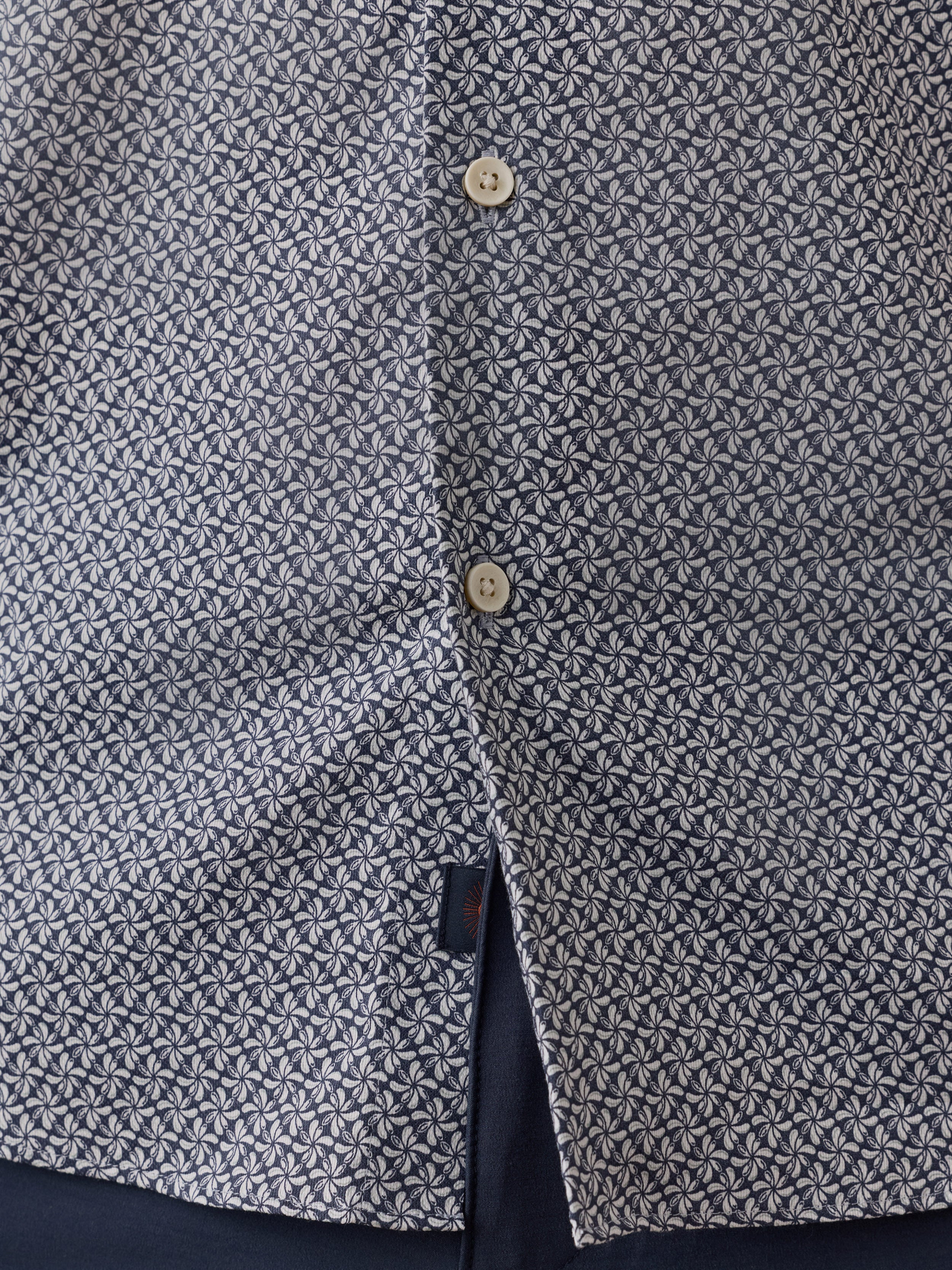 Close-up of a man wearing a patterned button-front shirt with a small geometric print in dark gray and off-white, plus visible buttons and a Faherty brand label near the hem
