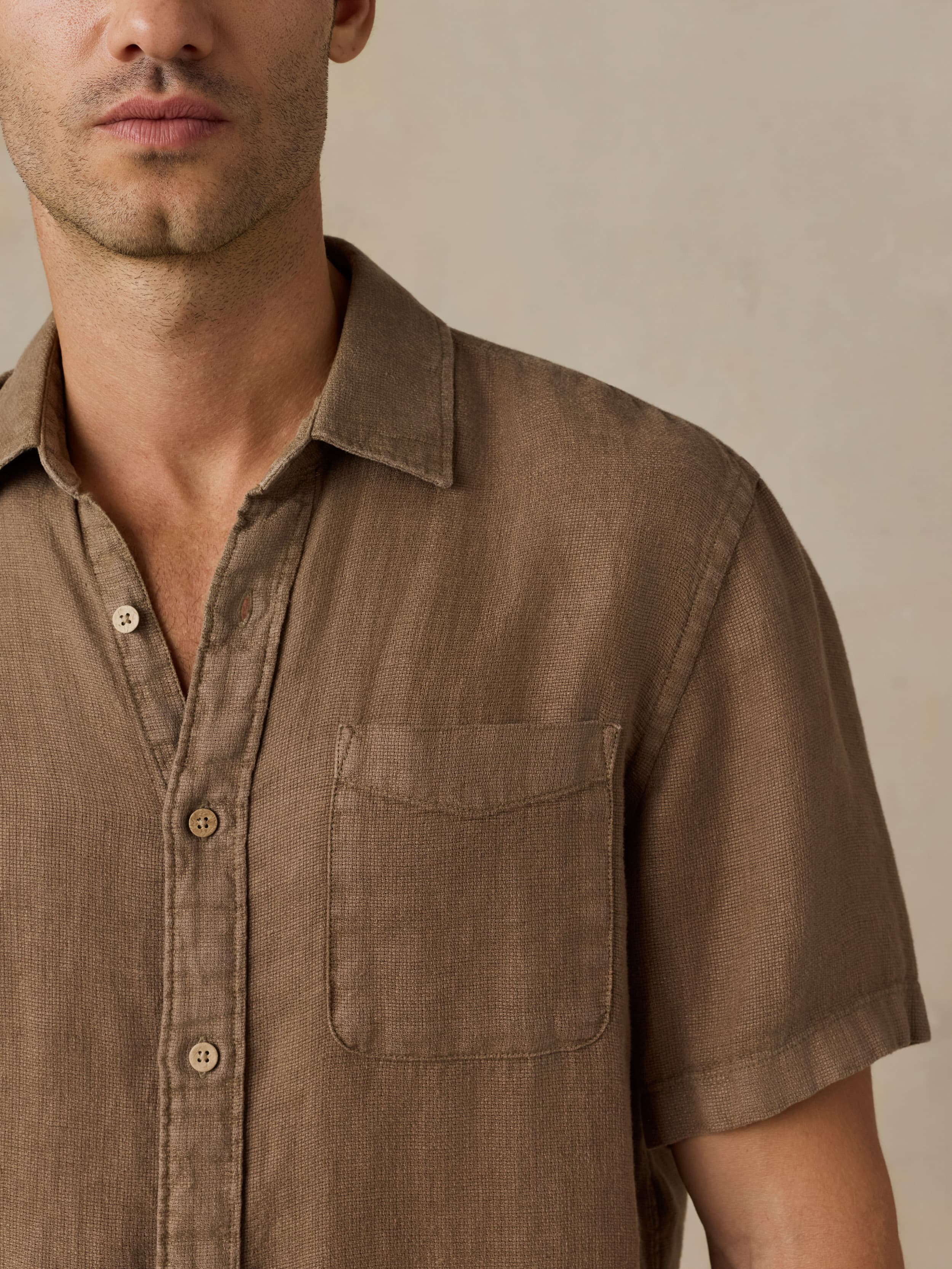 Man wearing a brown short-sleeve shirt against a beige background