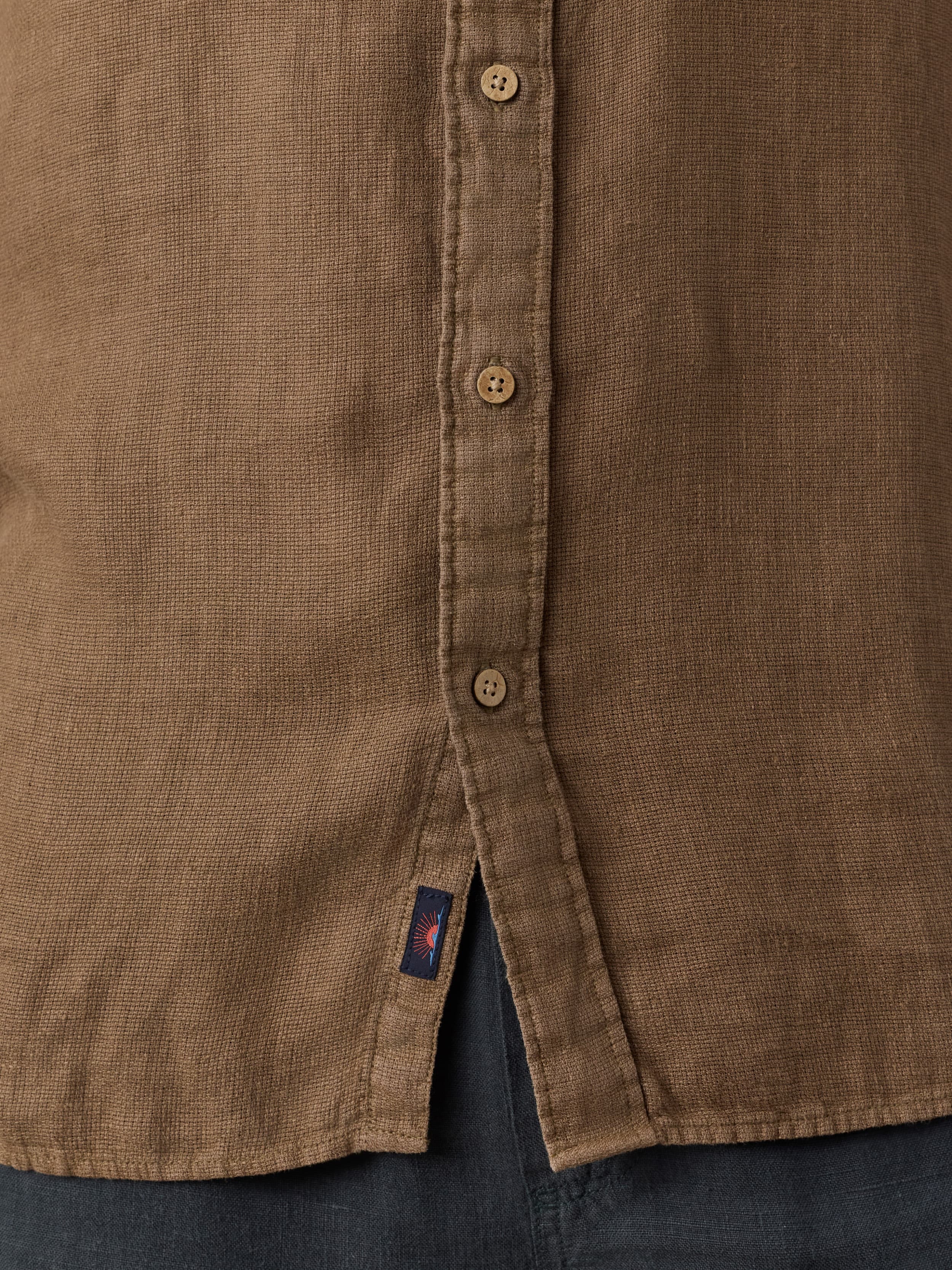 Close-up of a brown button-up shirt with a Faherty brand logo on a dark background