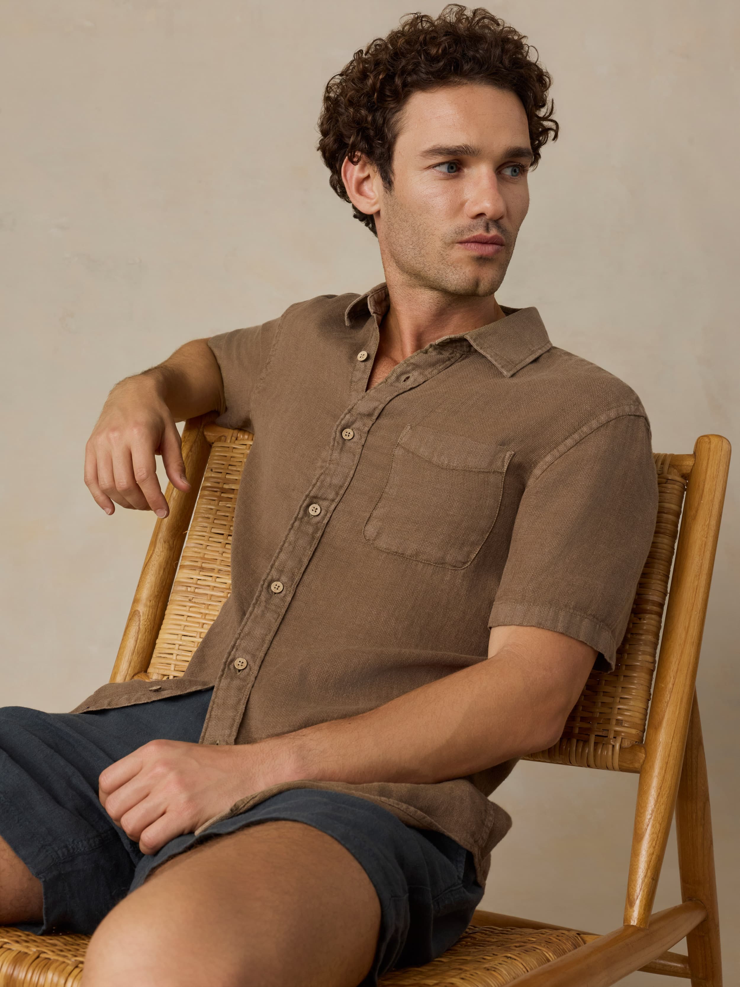 Man wearing a brown short-sleeve shirt and dark shorts against a beige background