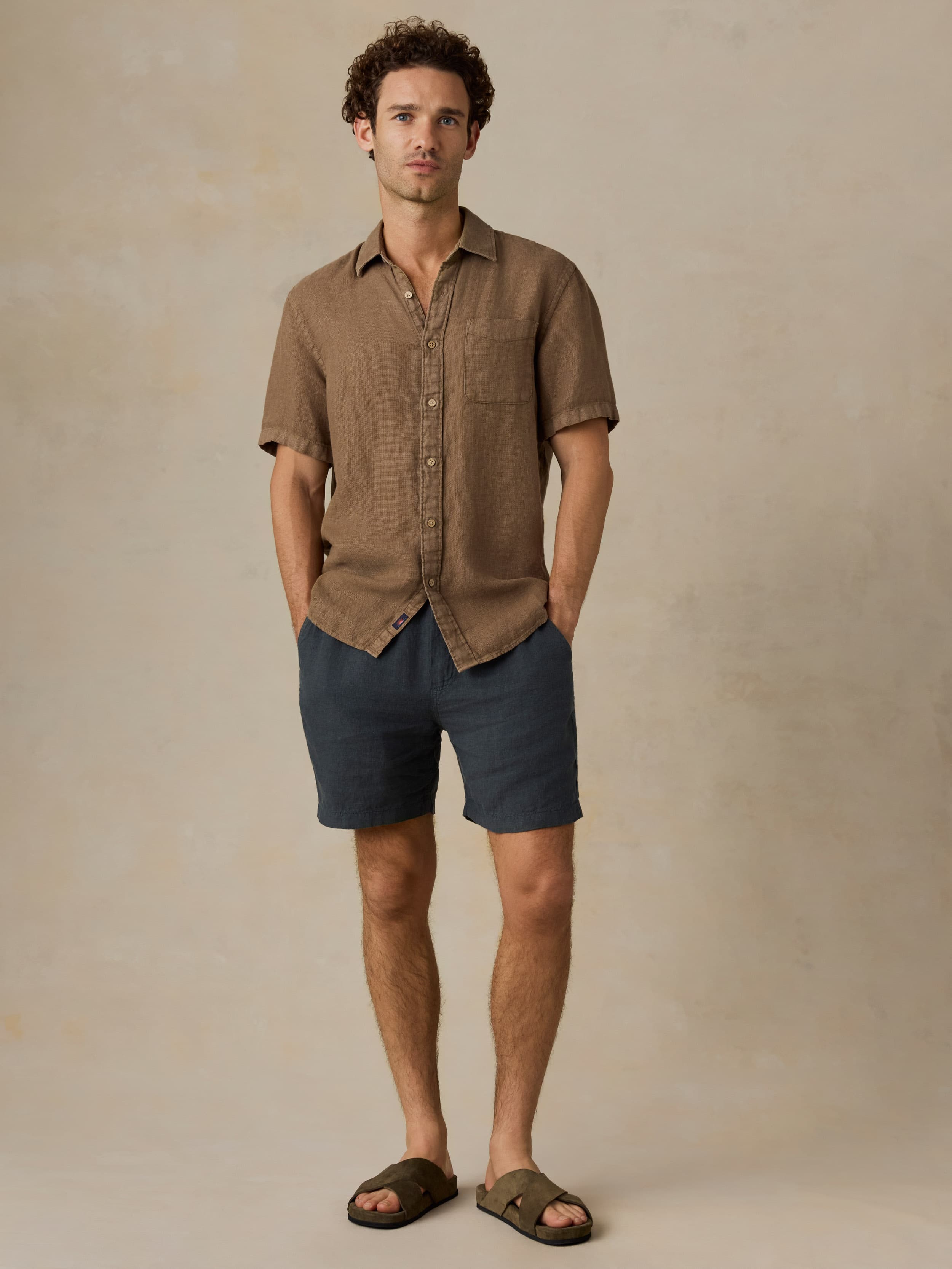 Man wearing a brown short-sleeve shirt and dark shorts against a beige background