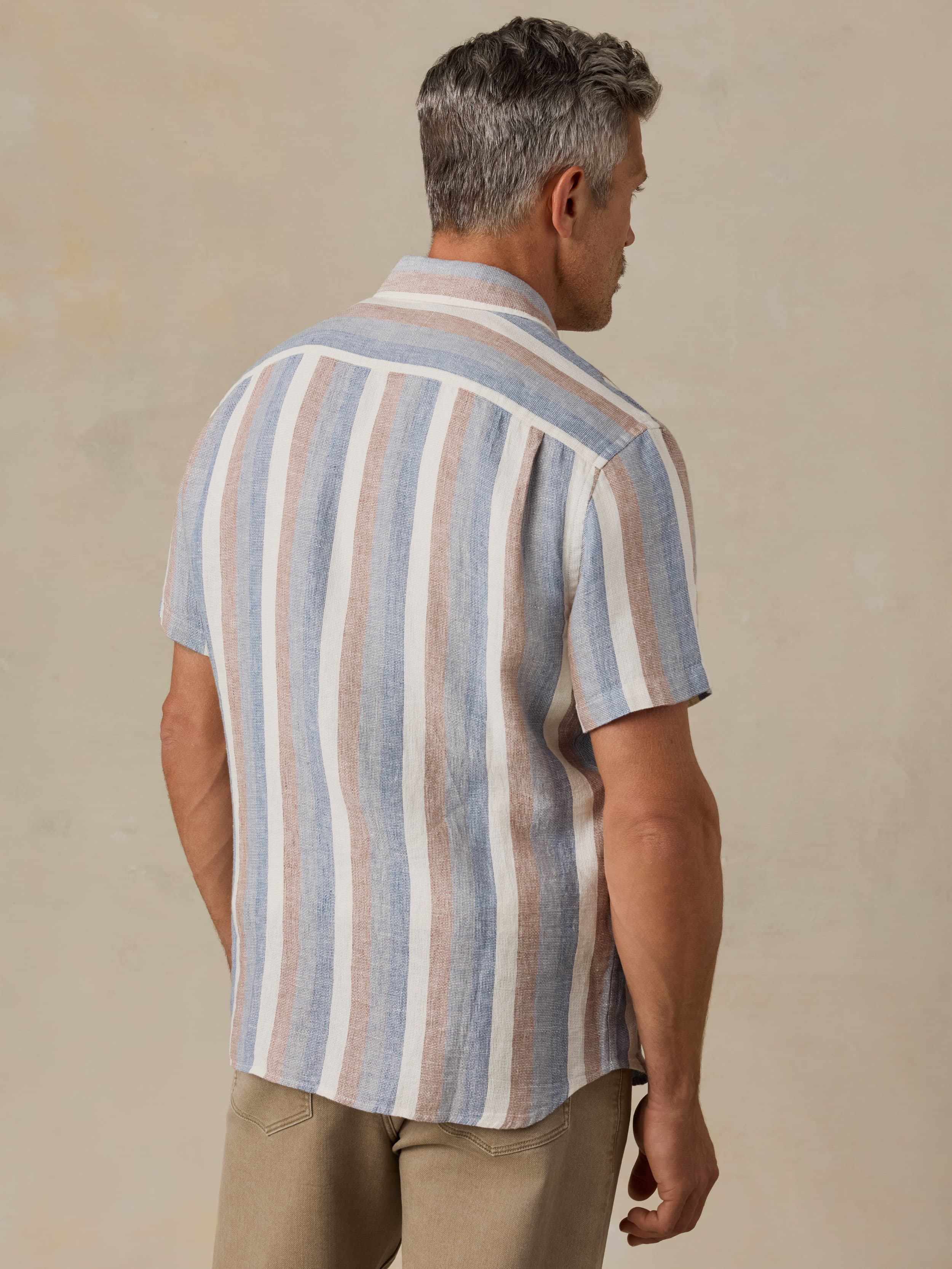 Man wearing a striped shirt and beige pants against a neutral background