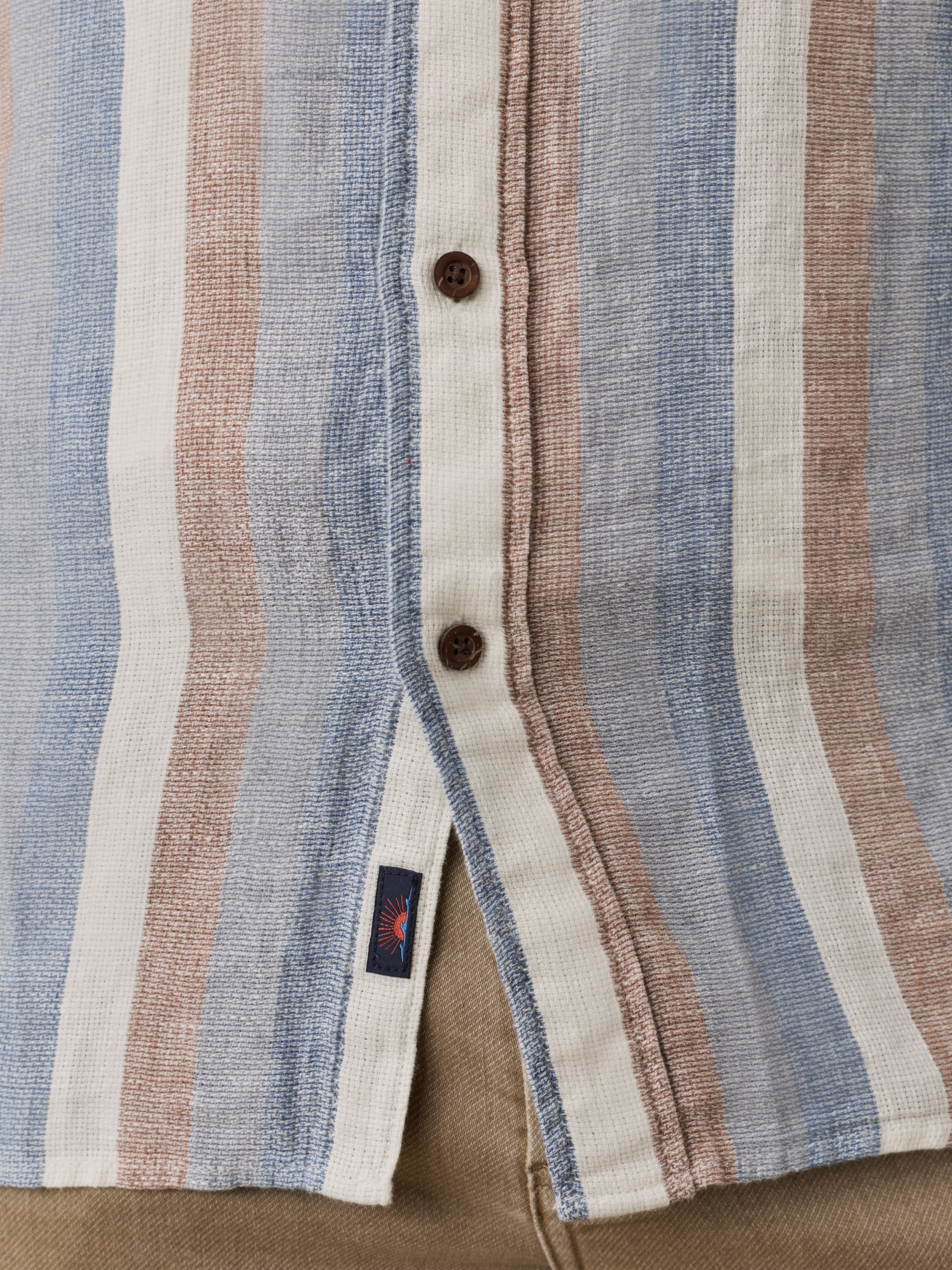 Close-up of a striped shirt with a button front placket and Faherty brand label near the hem