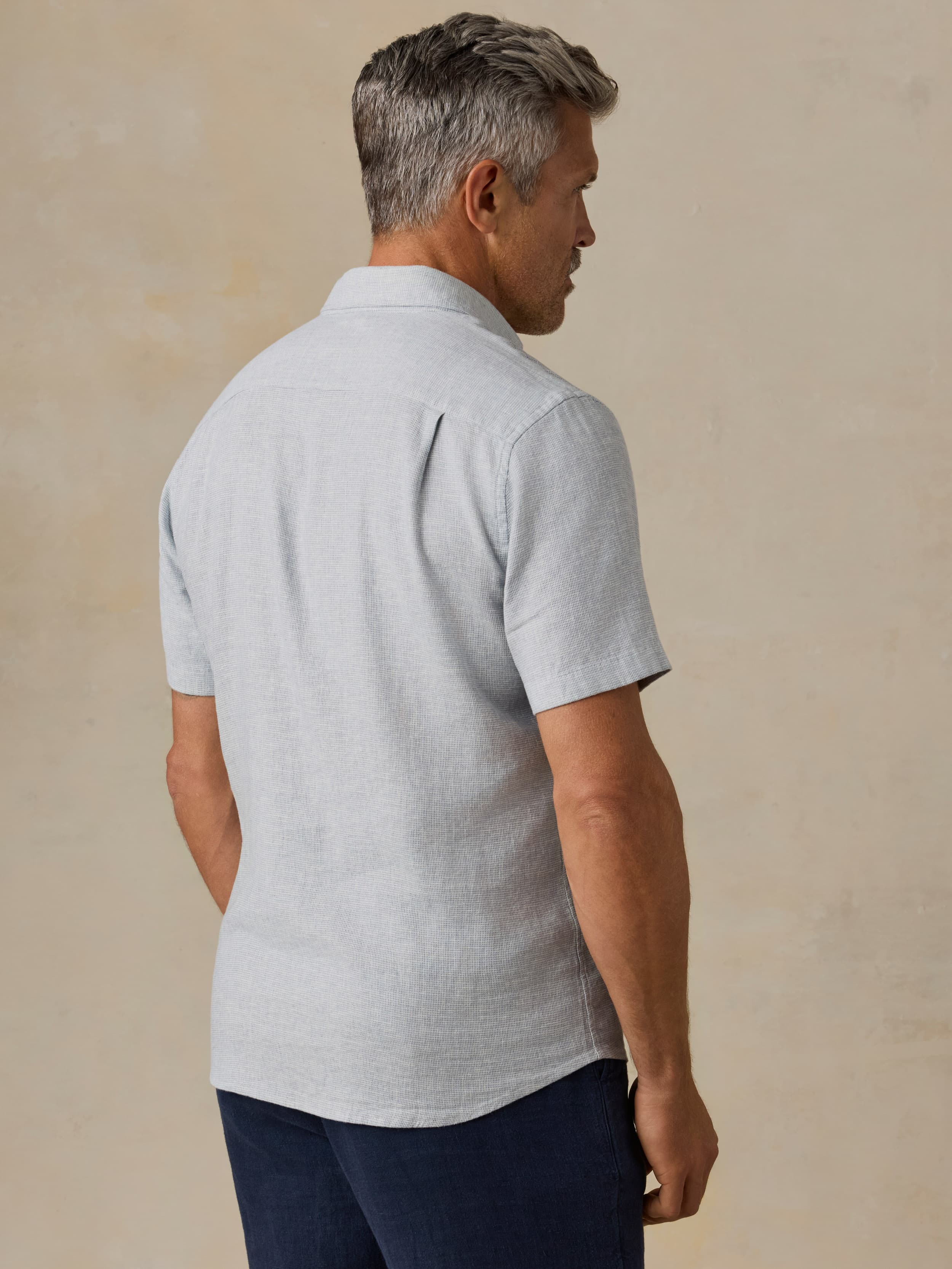 Man wearing a light blue short-sleeve shirt and dark blue pants against a beige background