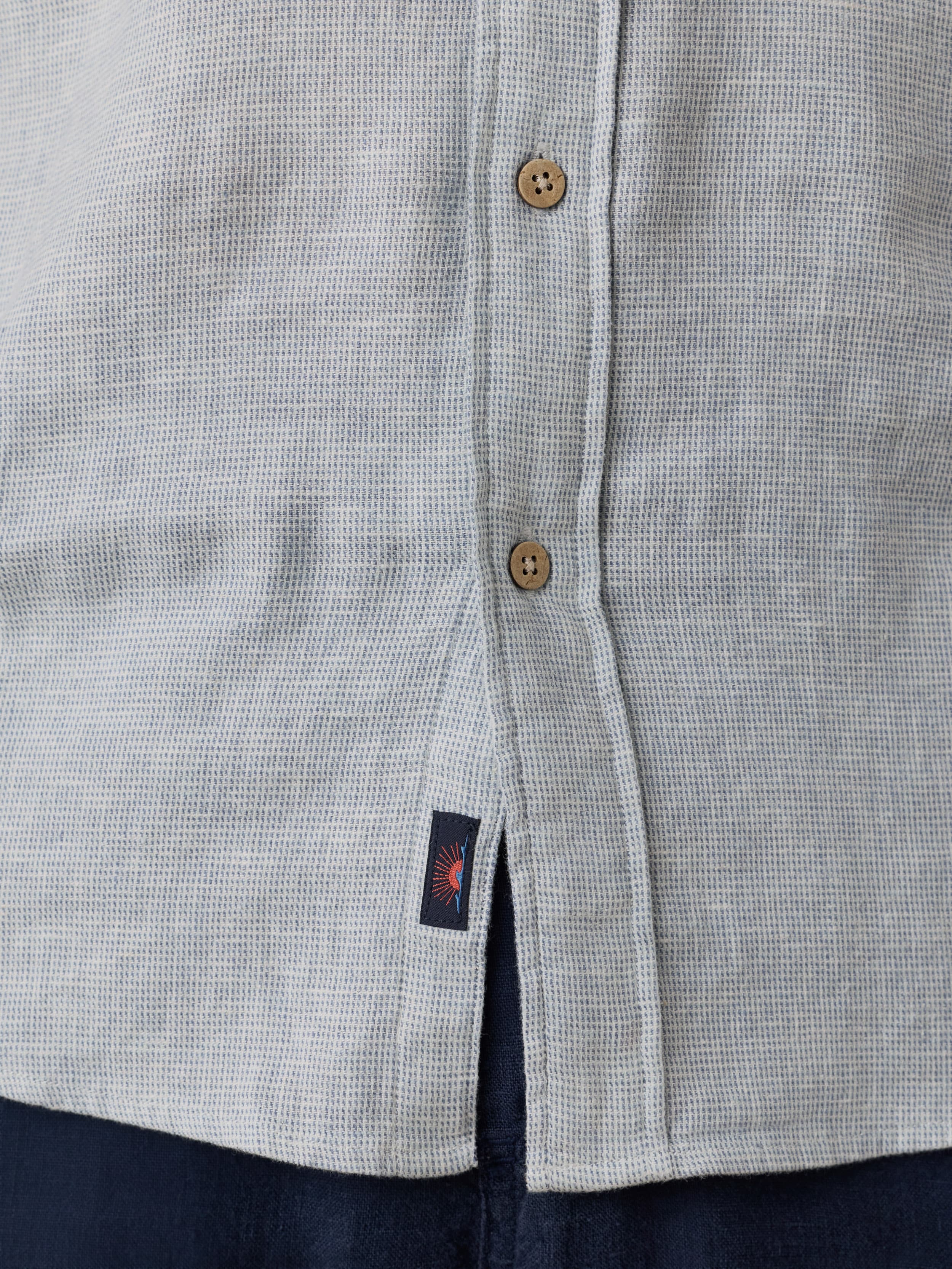 Close-up of a light blue short sleeve shirt with a visible Faherty brand logo near the hem