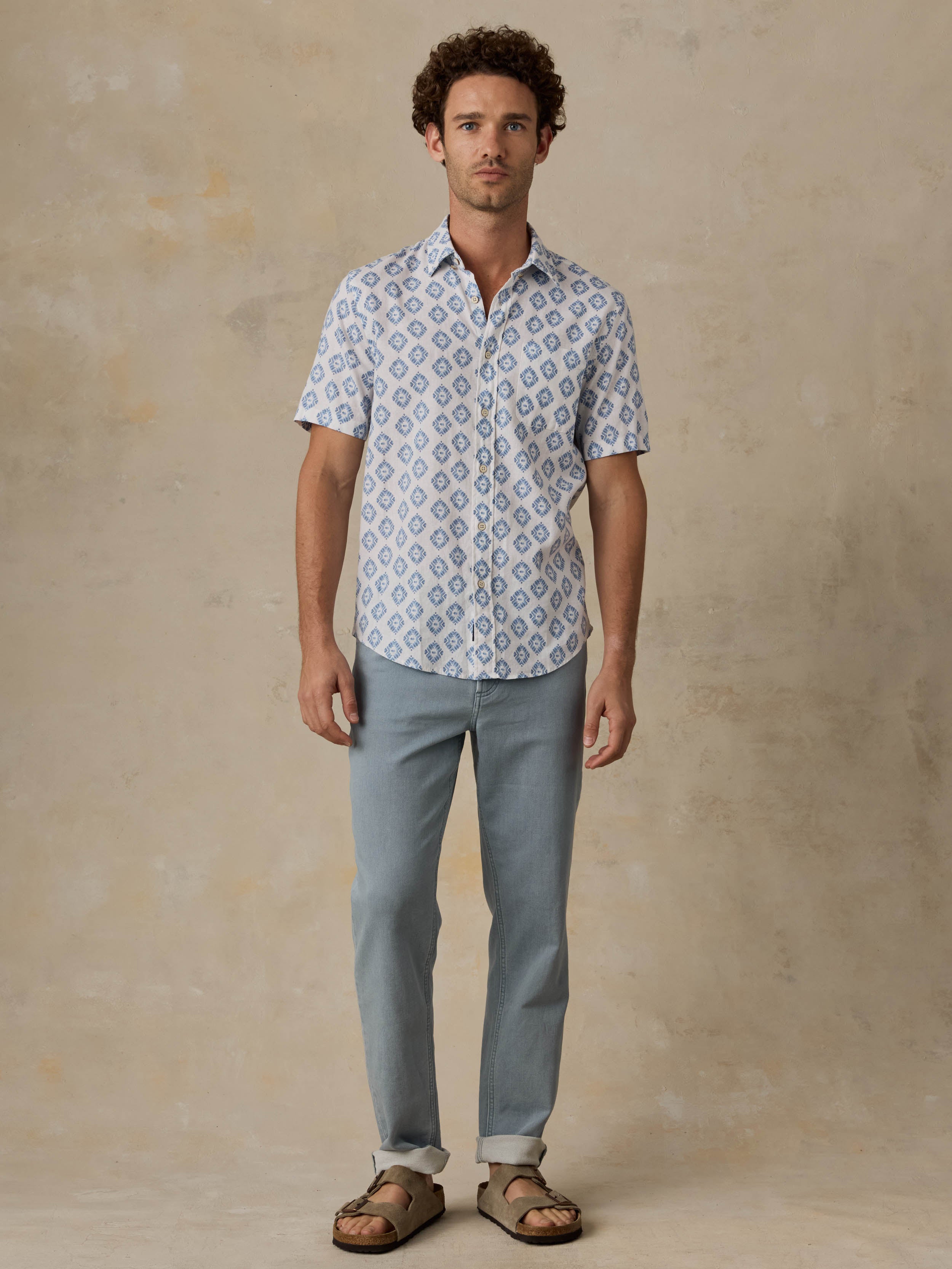 Man wearing a white and blue patterned shirt and light blue jeans against a beige background