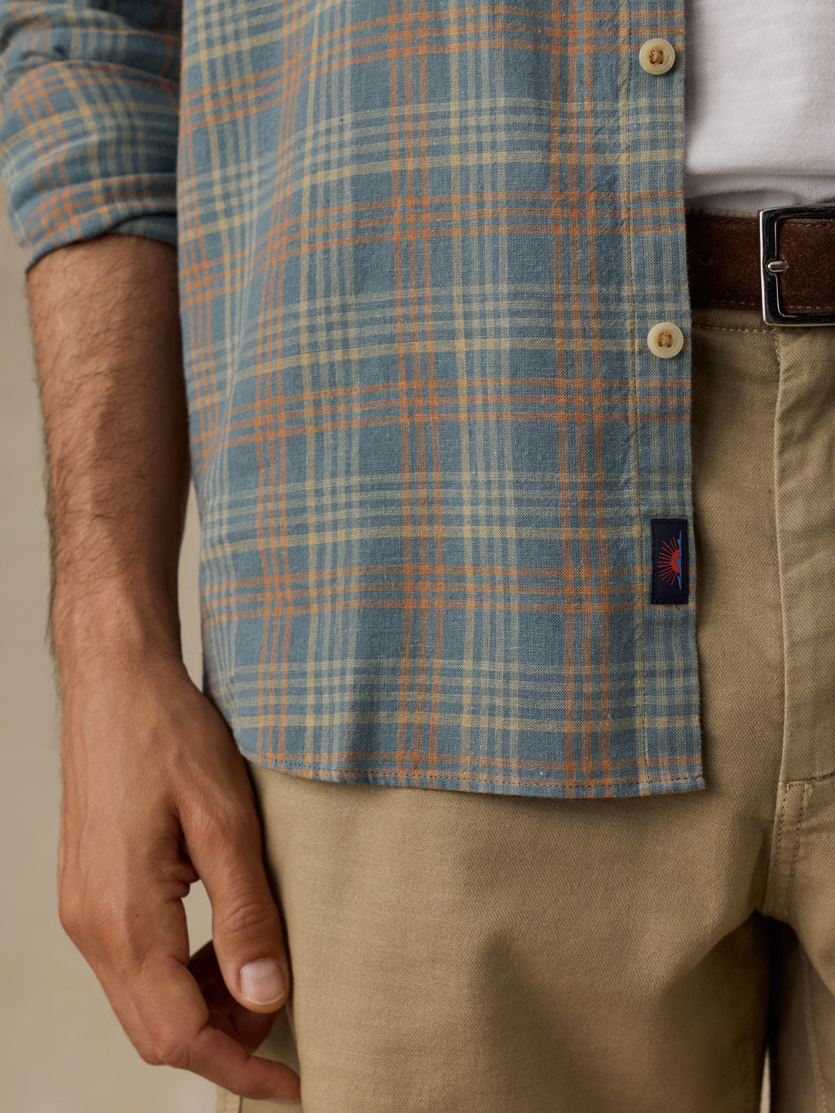 Close-up of a man wearing a blue and orange plaid button-down shirt over a white undershirt, paired with khaki pants and a brown belt., image 4 of 6