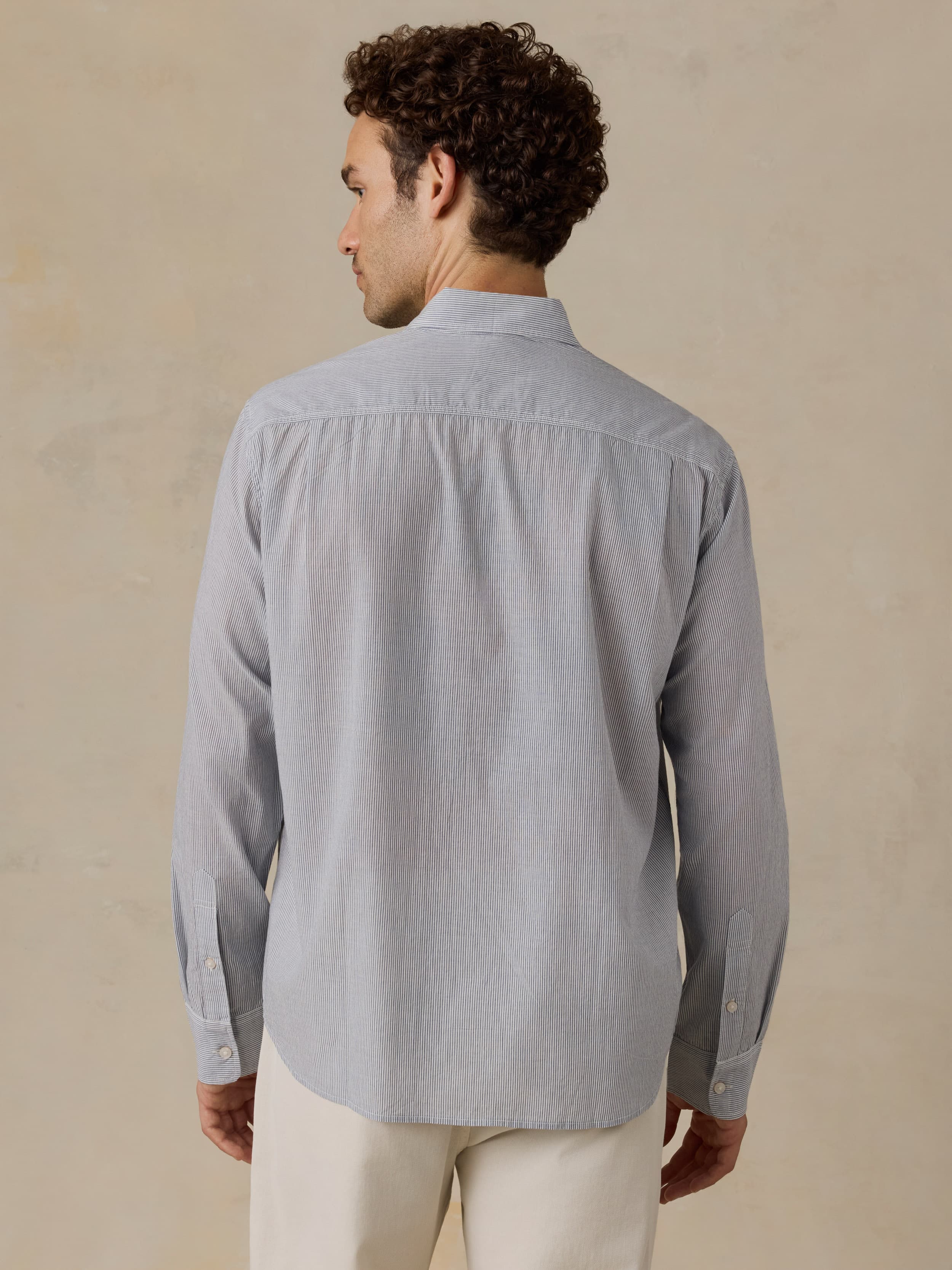 Man wearing a light blue shirt and white pants against a beige background