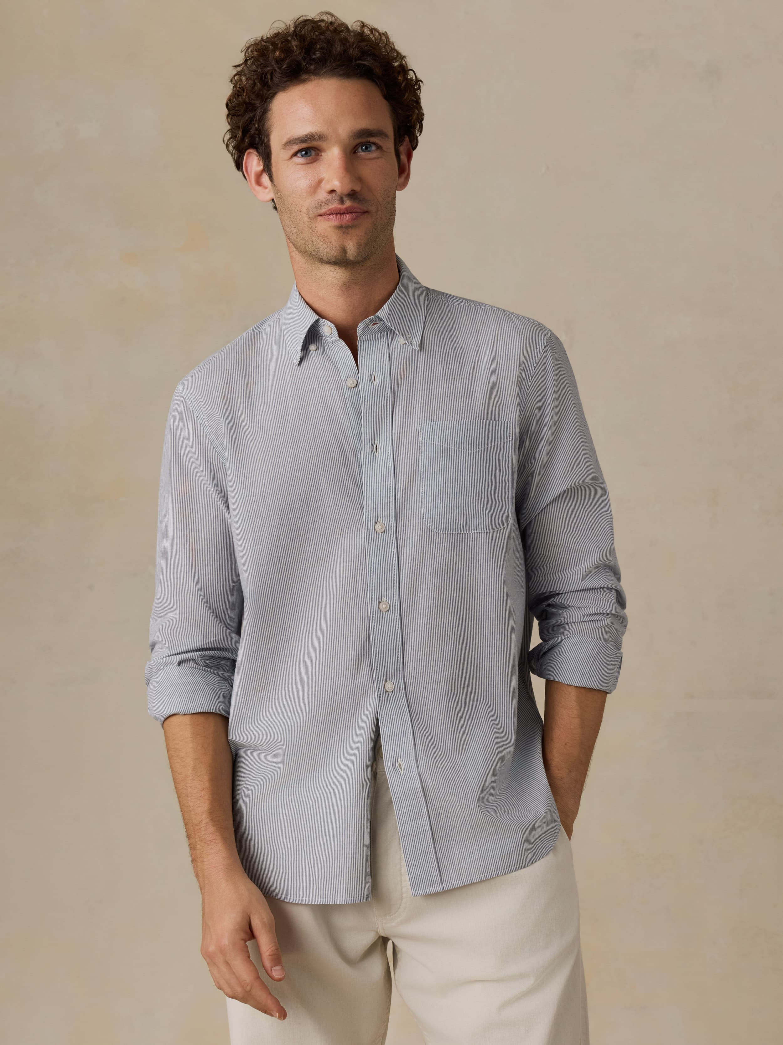 Man wearing a light blue shirt and white pants against a beige background