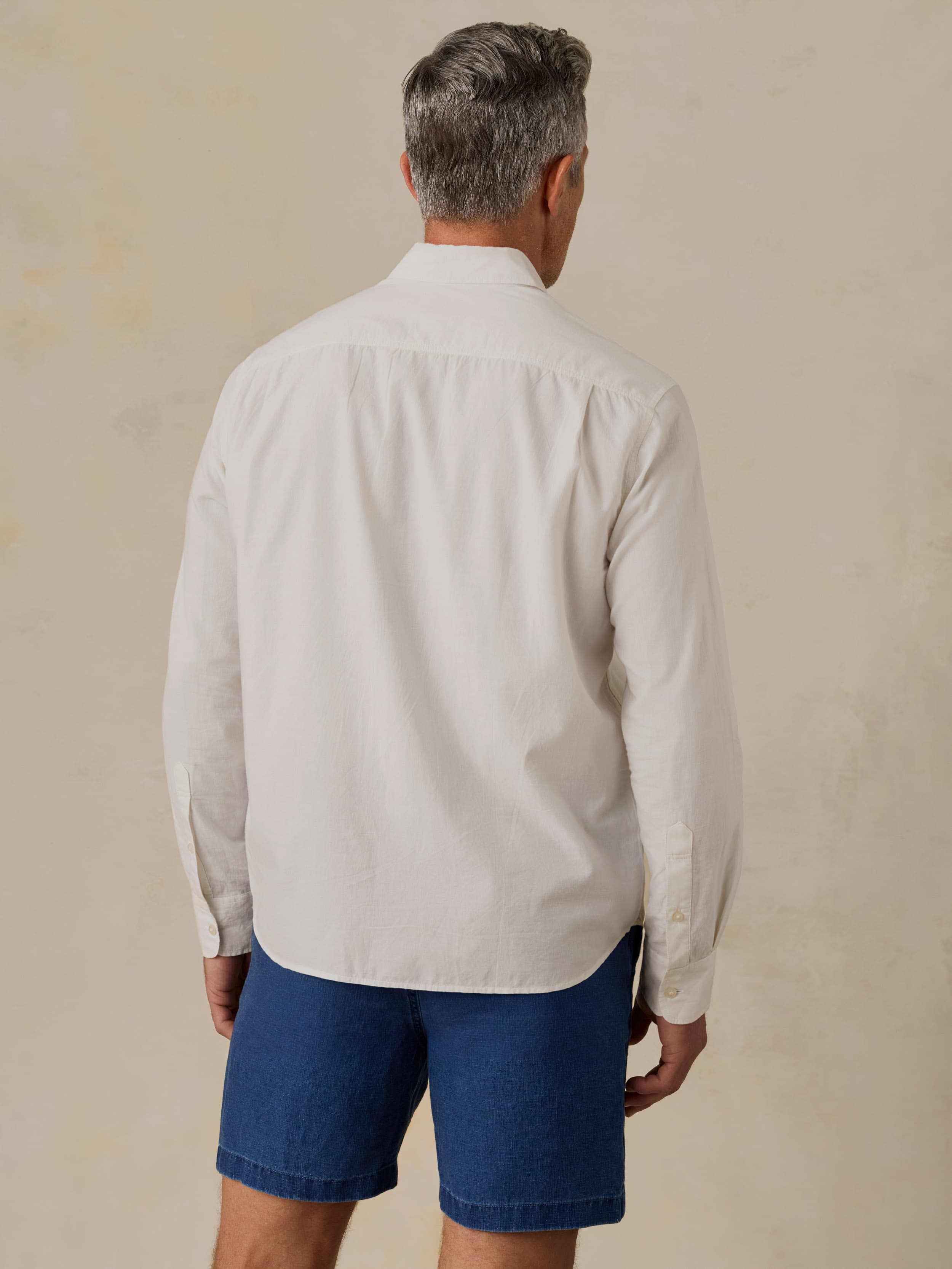 Man wearing a white button-up shirt and blue shorts against a beige background