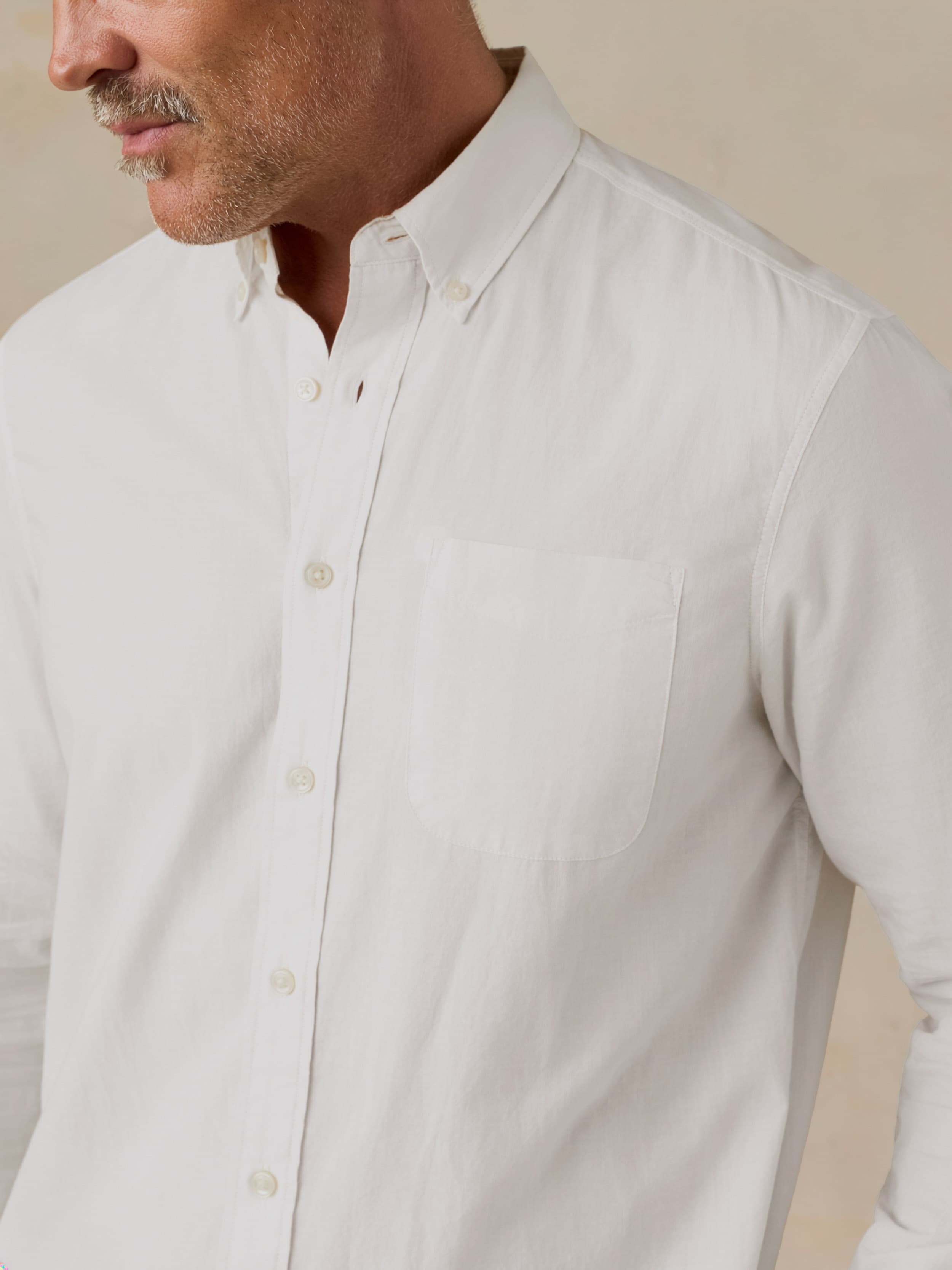 Man wearing a white button-up shirt against a beige background