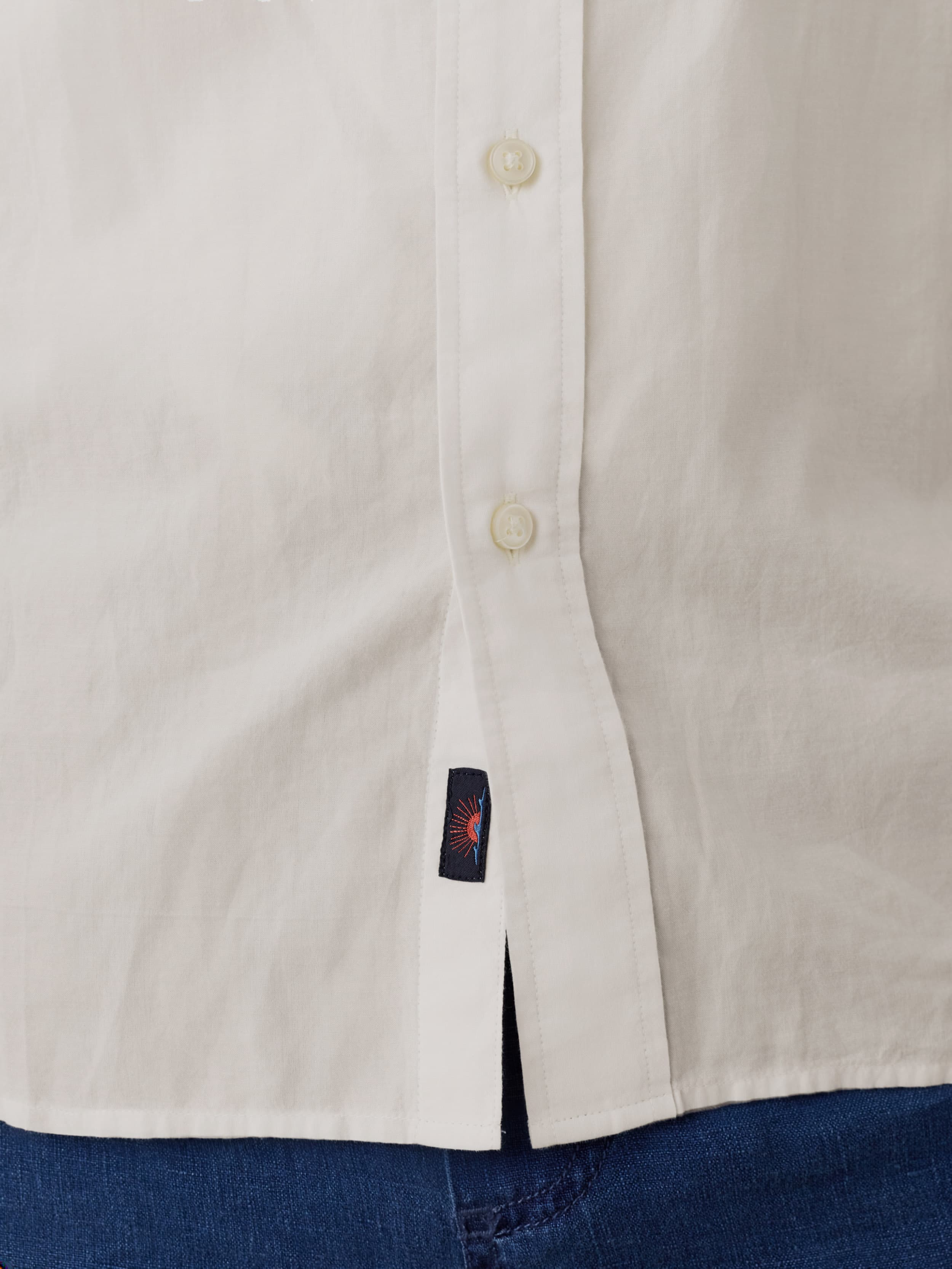 Close-up of a man wearing a white shirt with a Faherty brand label and blue shorts