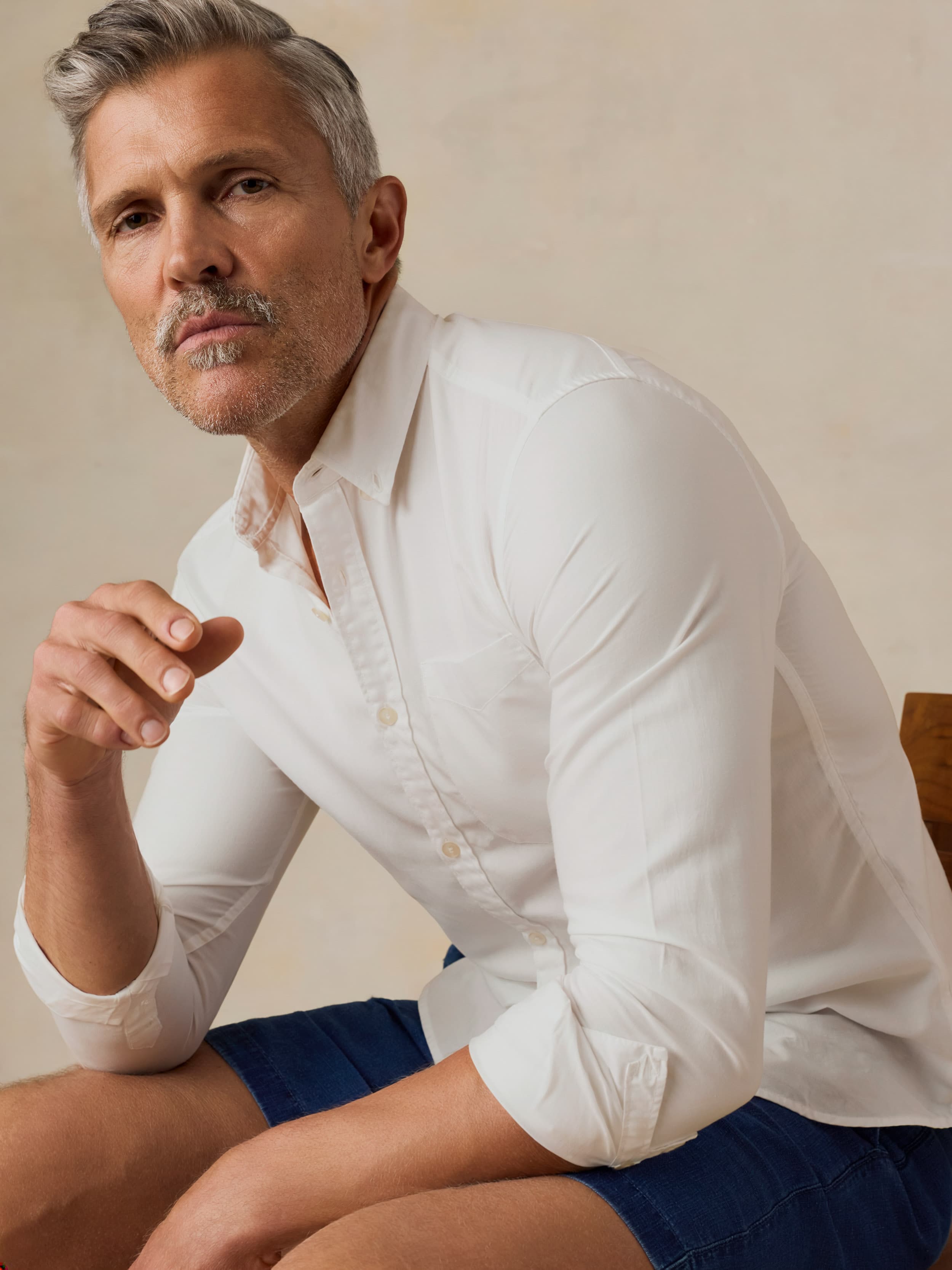 Man wearing a white button-up shirt and blue shorts against a beige background