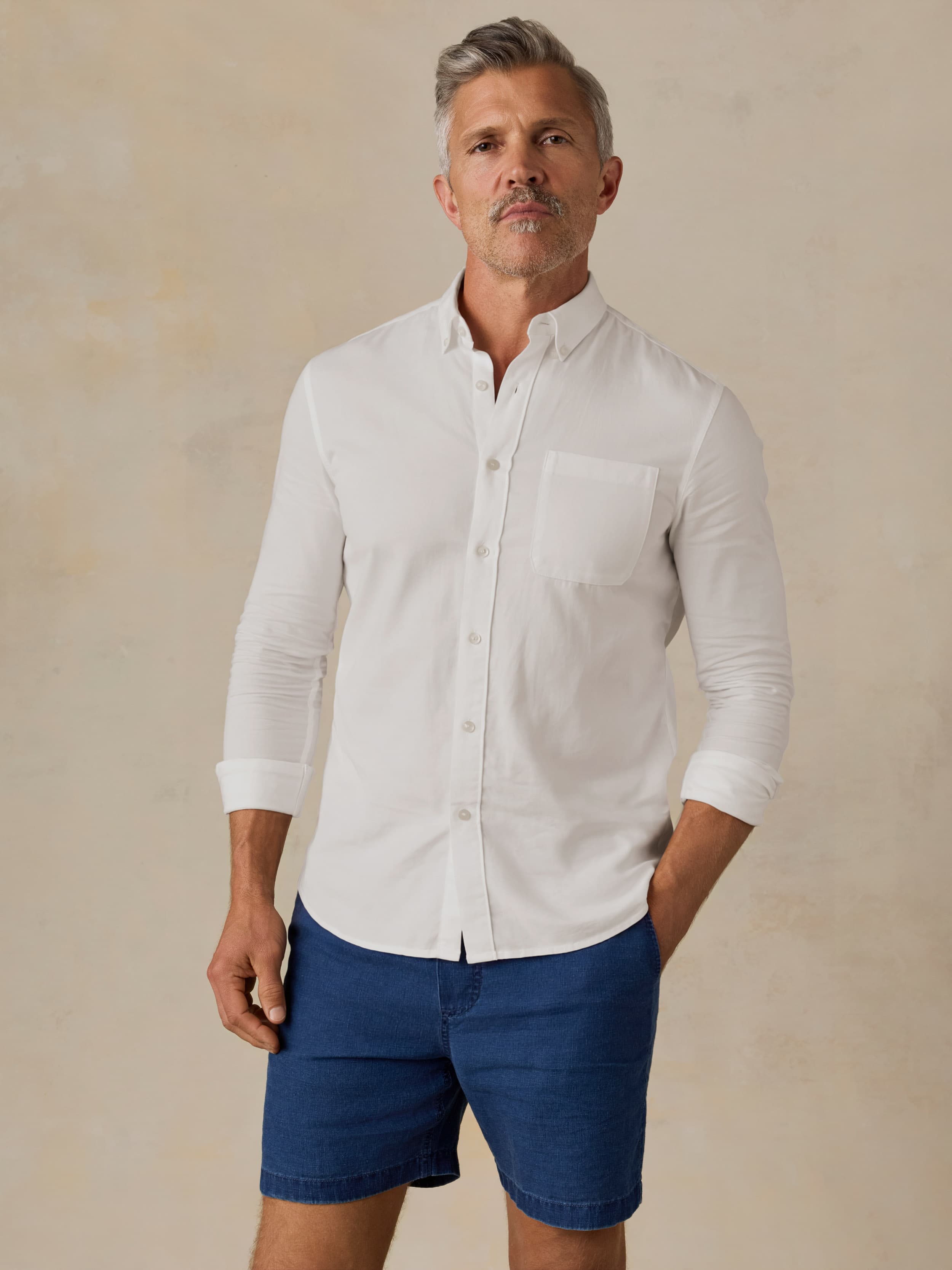 Man wearing a white button-up shirt and blue shorts against a beige background