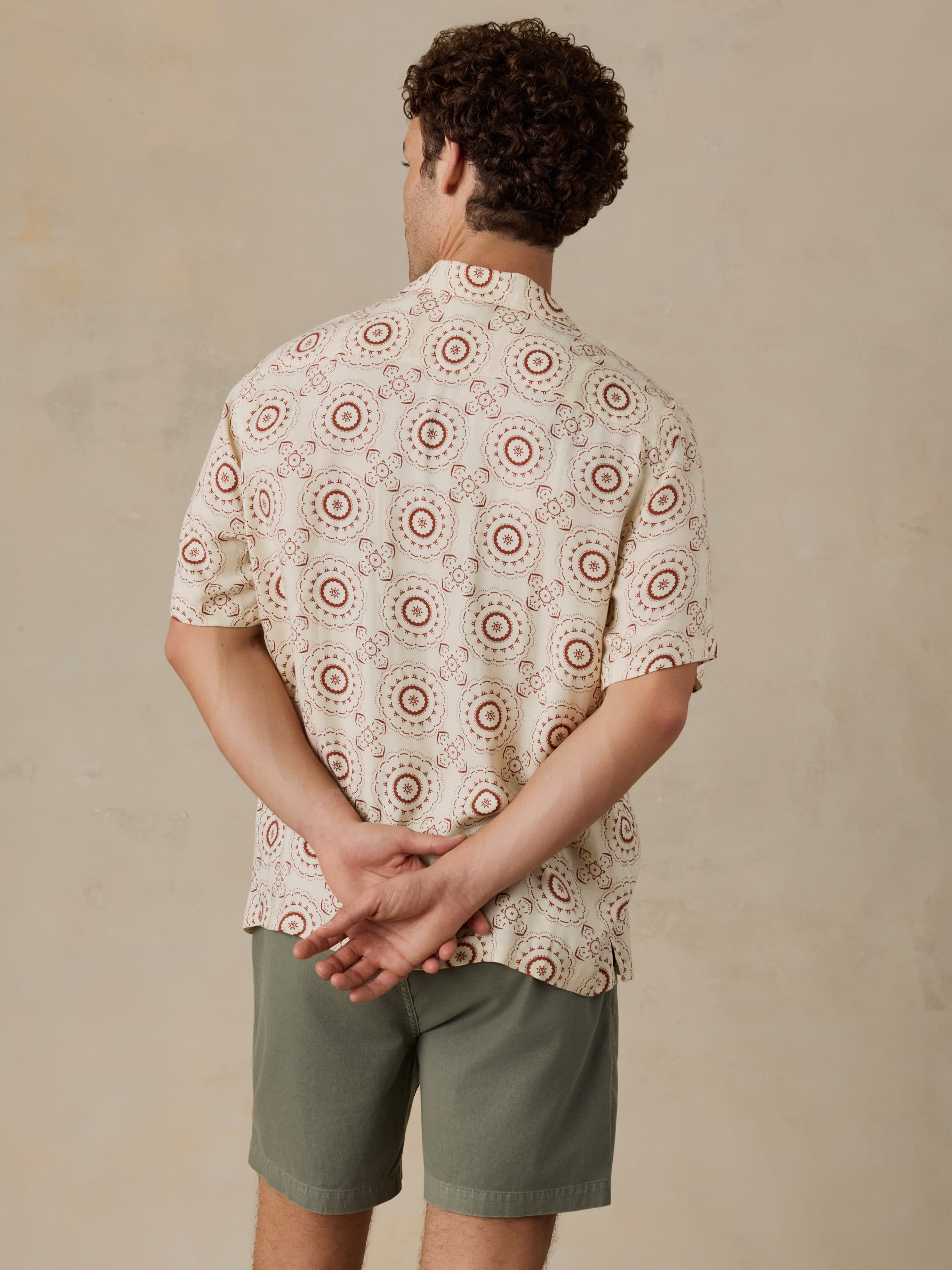 Man wearing a patterned shirt and green shorts against a beige background