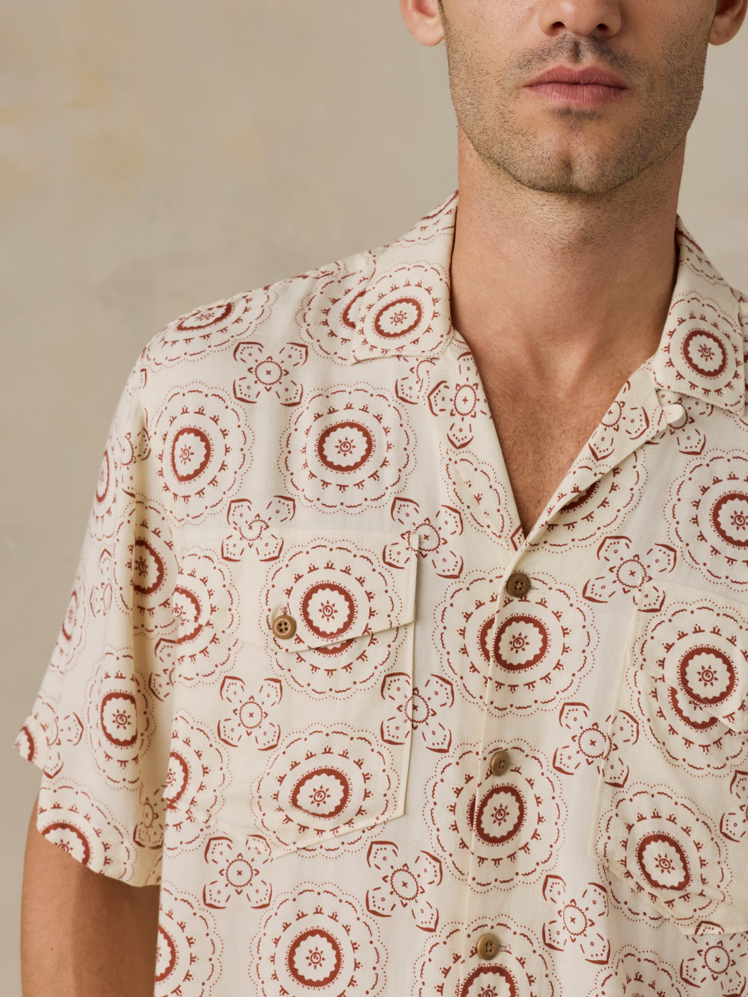 Man wearing a patterned shirt with red circular designs against a beige background