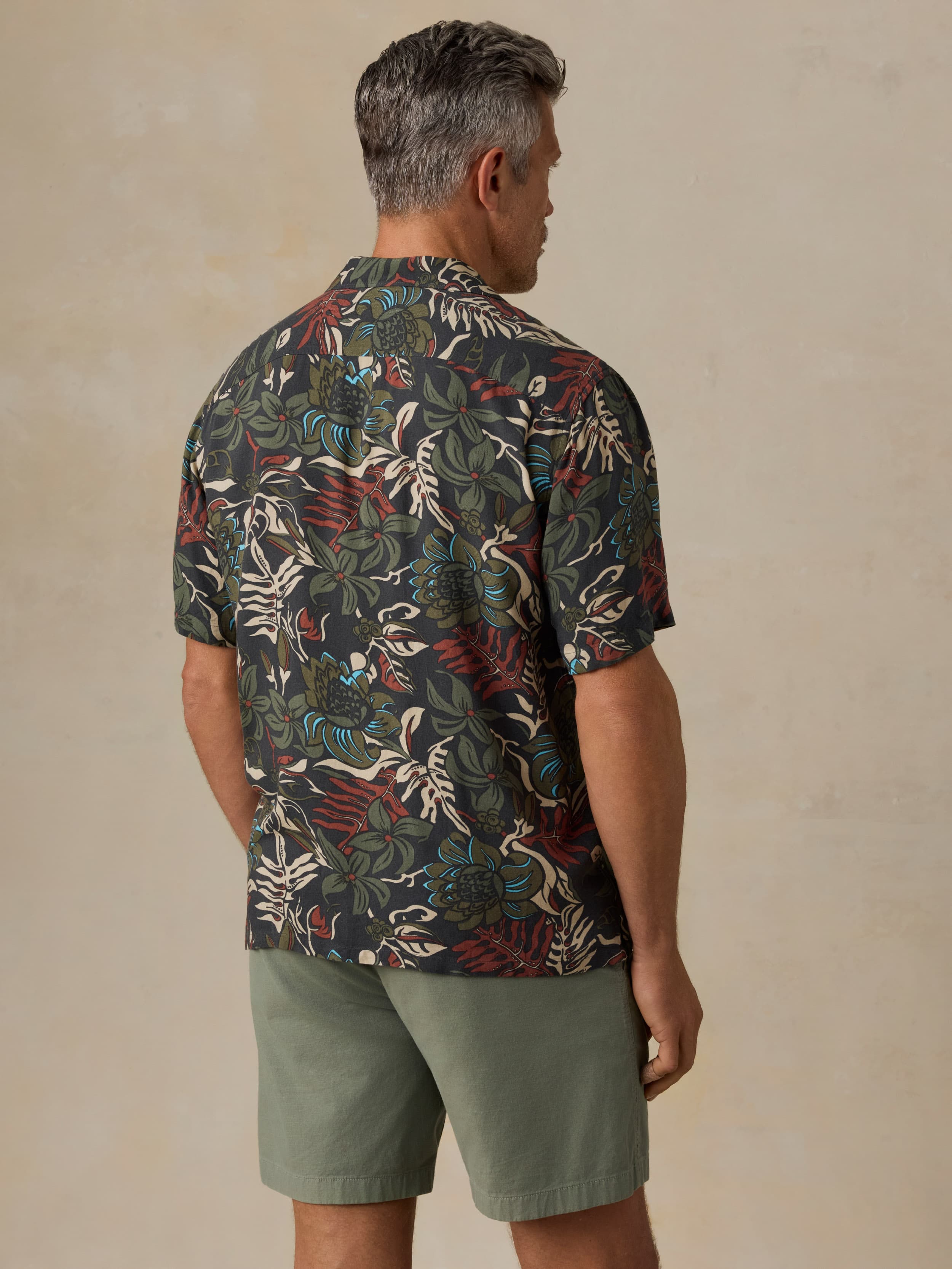 Man wearing a tropical patterned shirt and green shorts against a beige background
