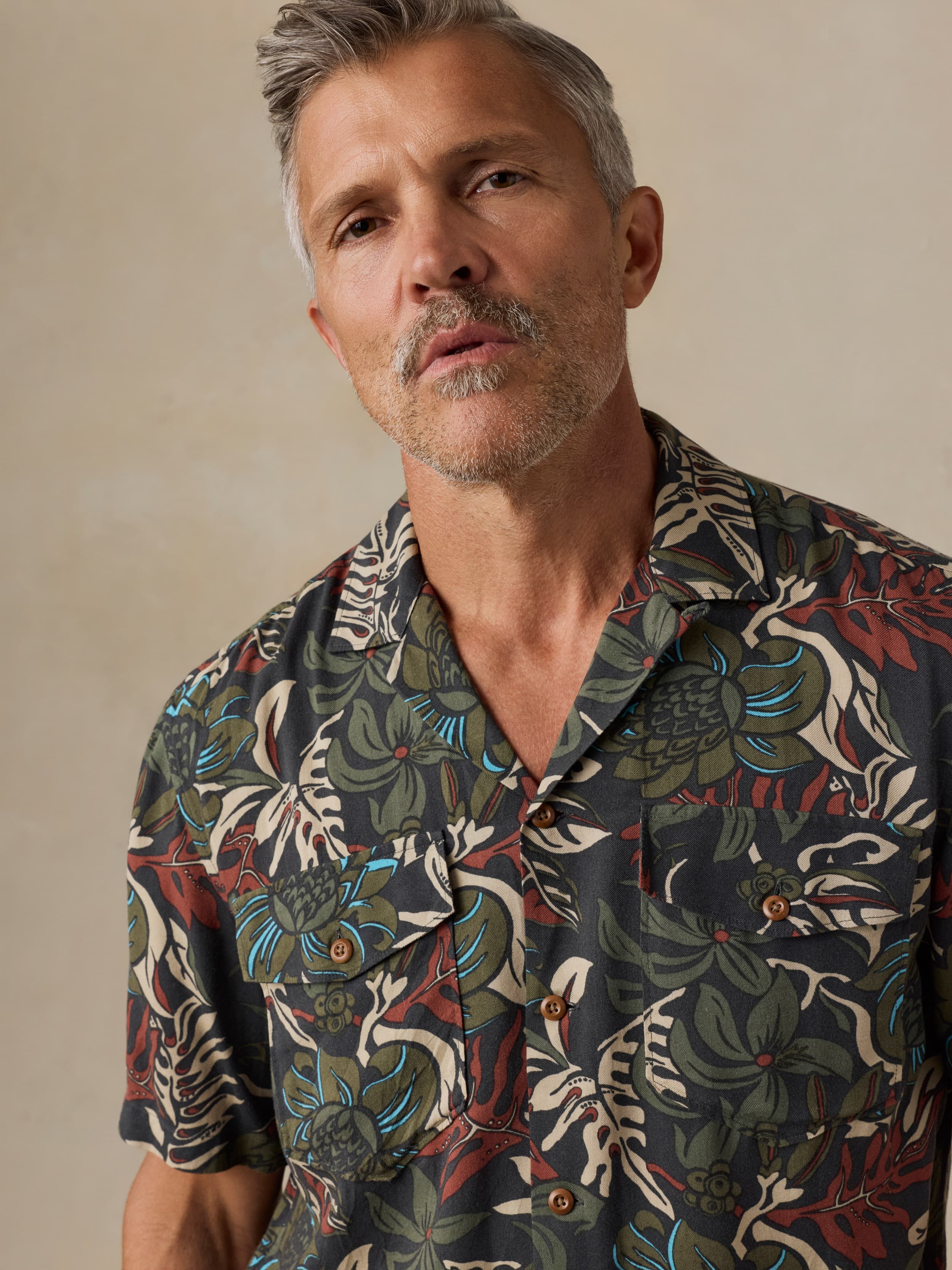 Man wearing a tropical patterned shirt against a beige background