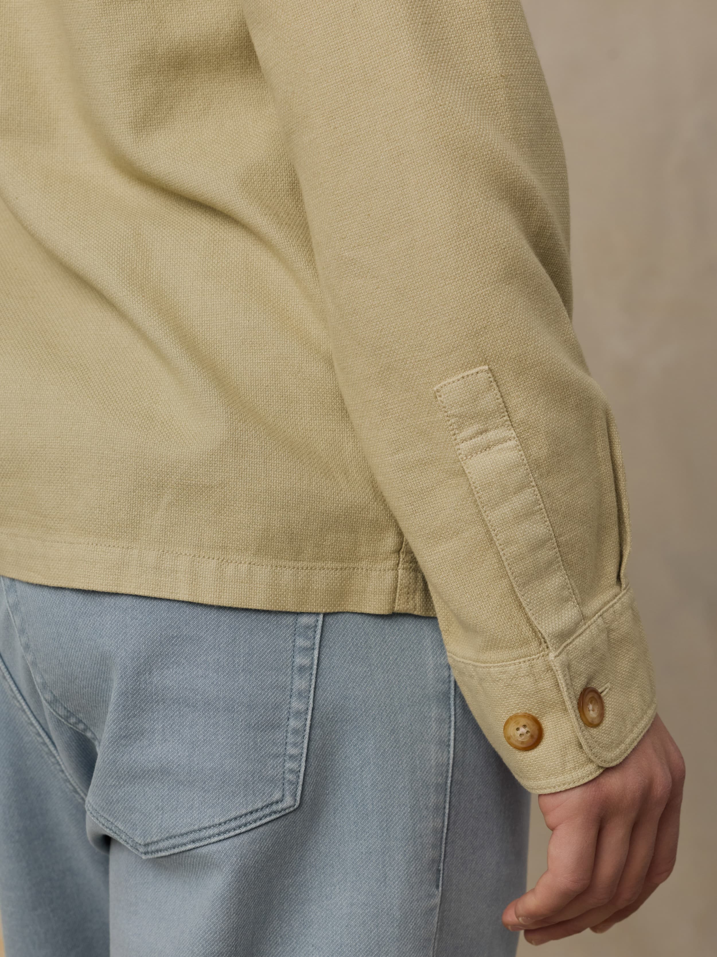 Beige shirt with button cuffs sleeves and blue jeans on a beige background