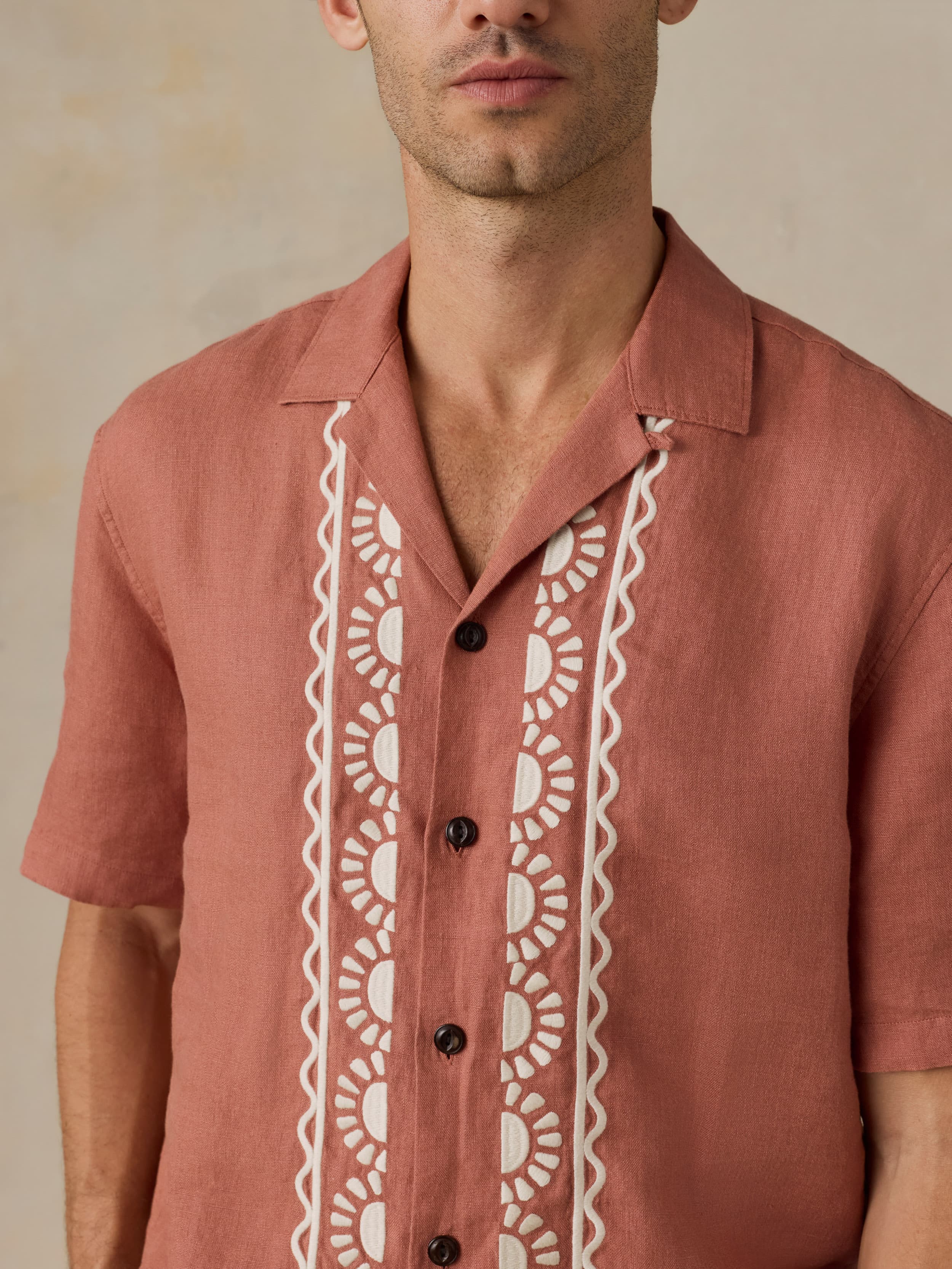 Man wearing a red shirt with embroidered white lace details on a beige background