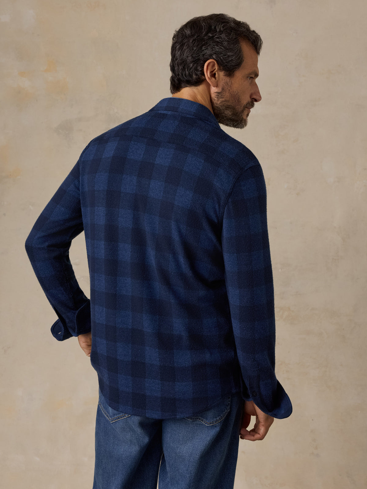 A man viewed from the back wearing a blue checkered flannel and blue jeans, image 2 of 5
