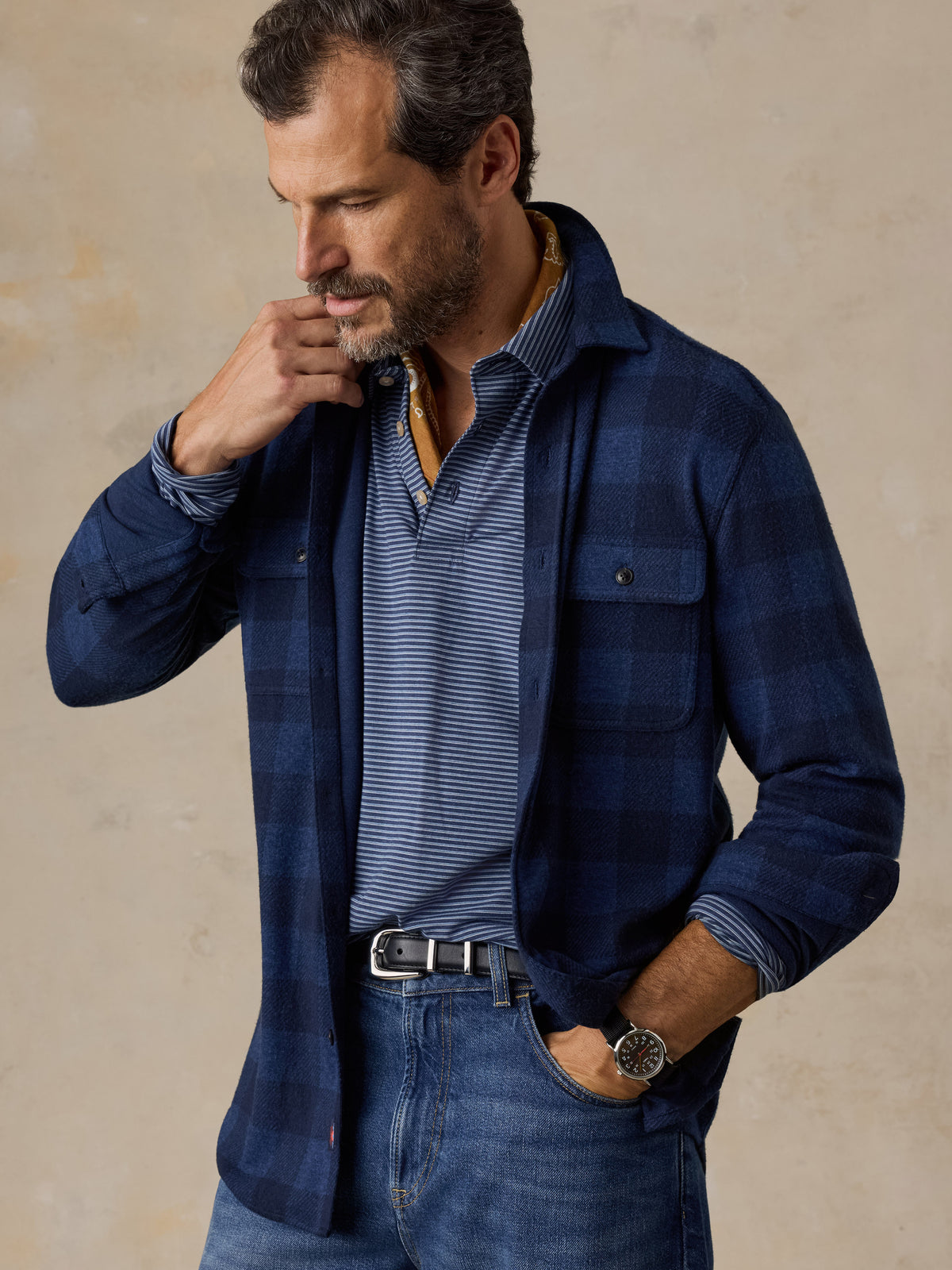 A man wearing a blue checkered flannel and blue jeans, image 4 of 5