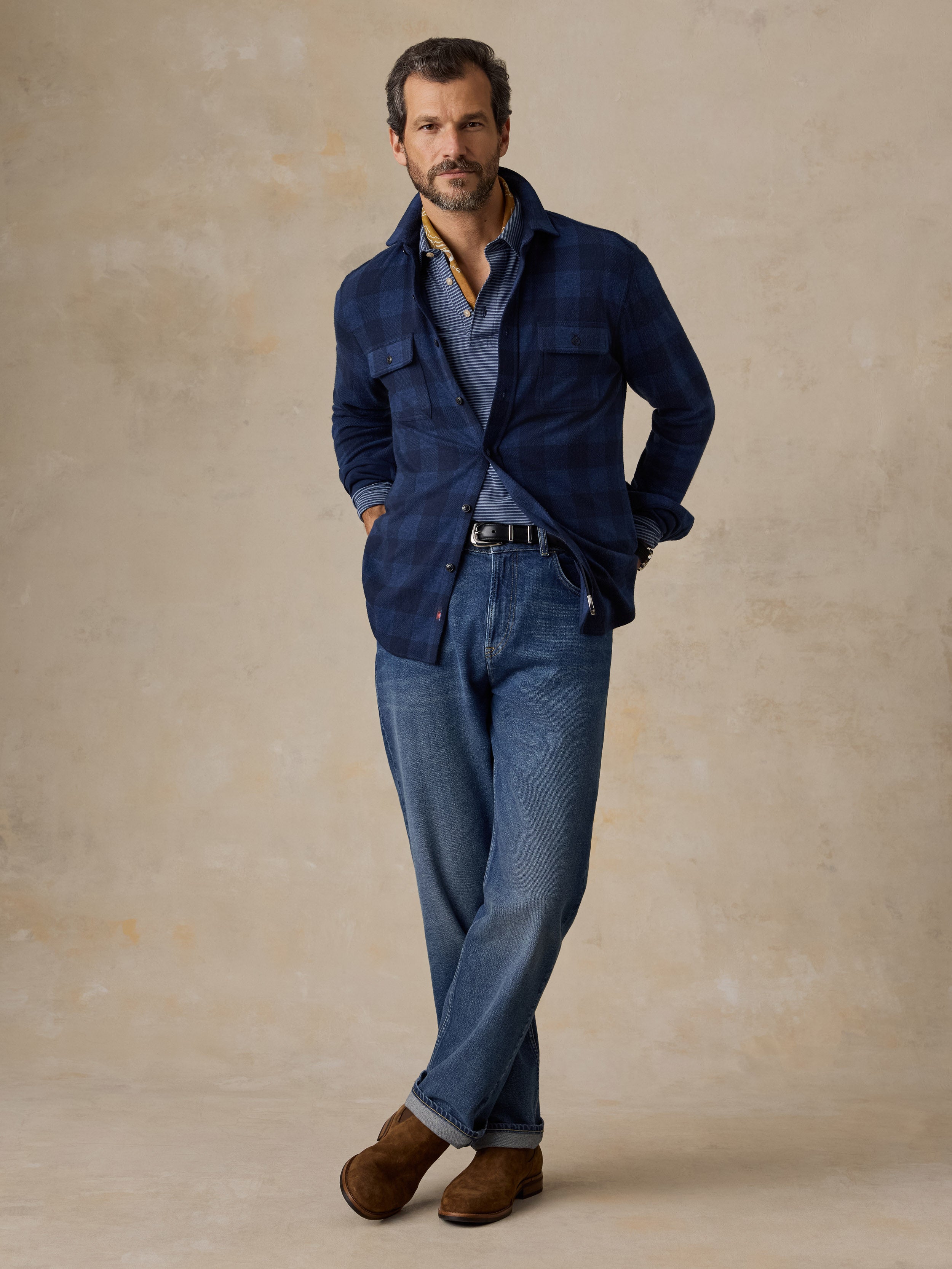 A man wearing a blue checkered flannel, blue jeans, and brown boots