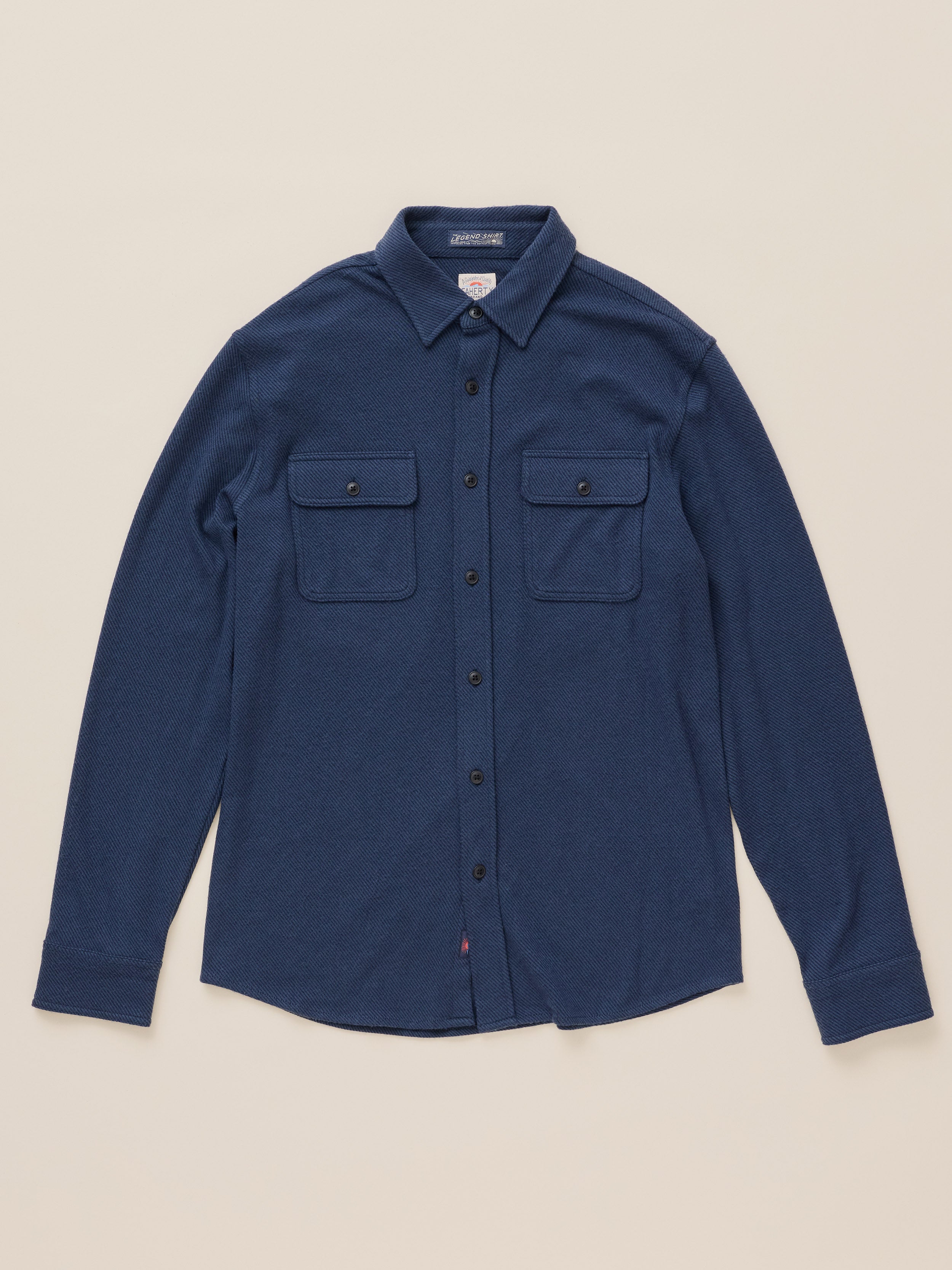 A dark blue long-sleeve button-up shirt with two buttoned chest pockets, laid flat on a light beige background.