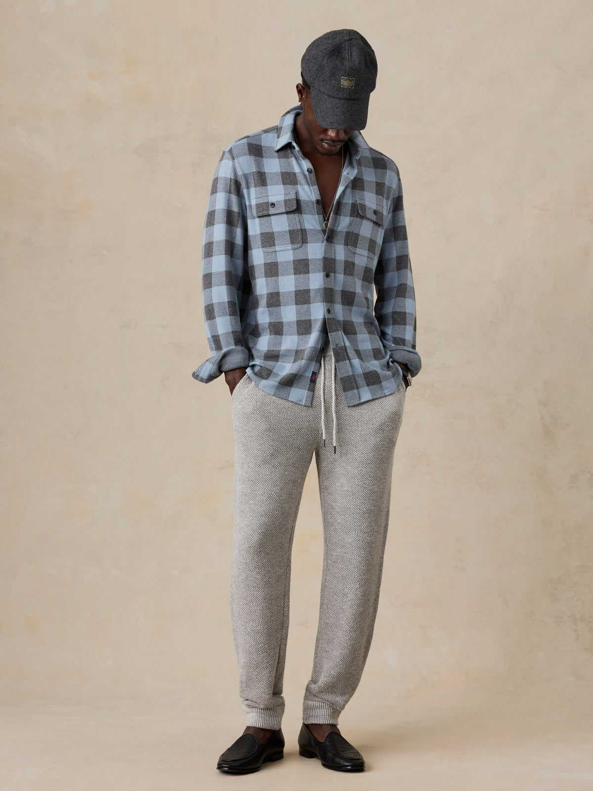 A man wearing a blue plaid shirt and sweatpants, image 2 of 5