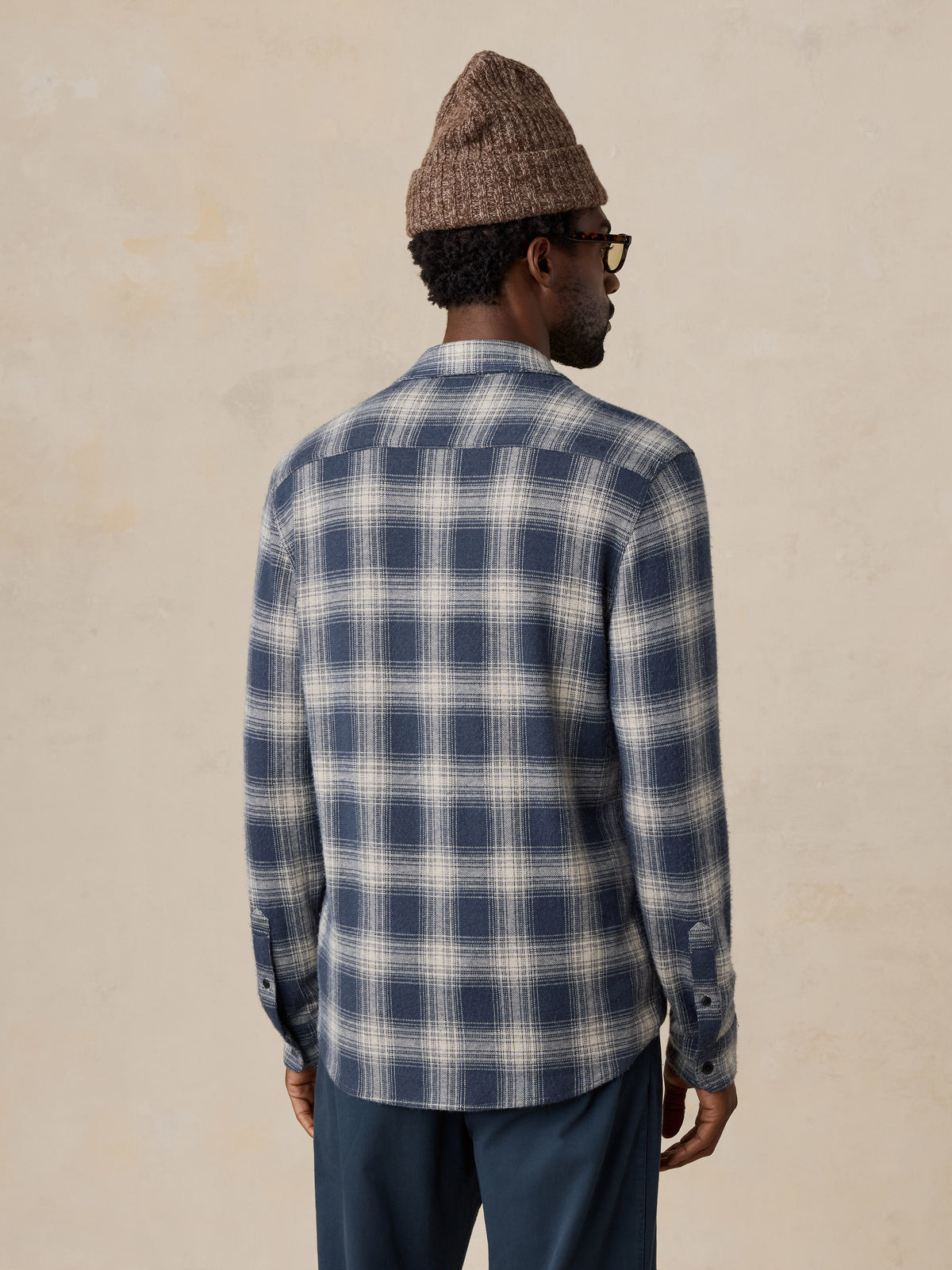 A man viewed from behind wearing a blue button up shirt and a brown beanie, image 5 of 5