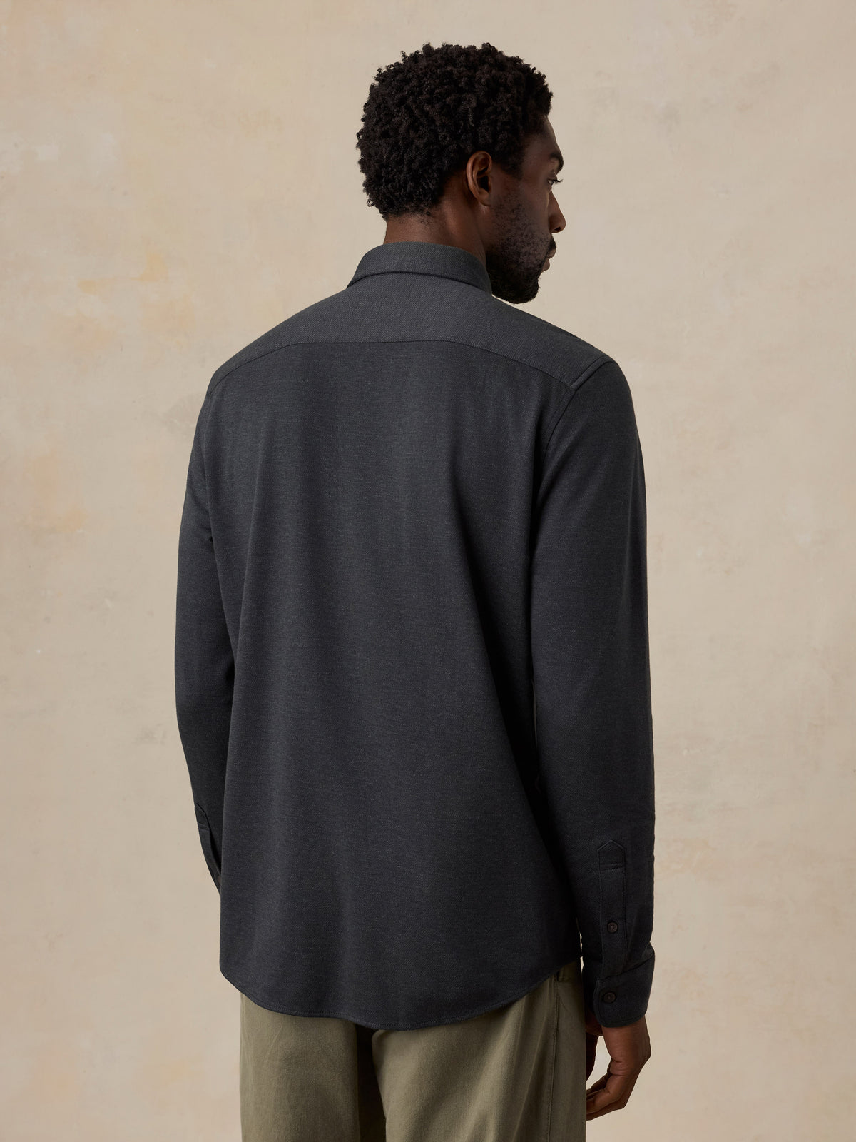 A man viewed from behind wearing a black shirt and green pants, image 3 of 6