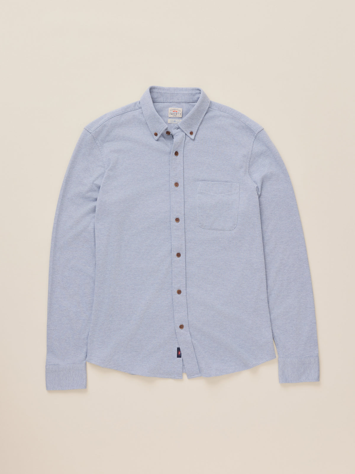 A light blue long-sleeve button-down shirt with a pointed collar and brown buttons, laid flat against a solid beige background.
