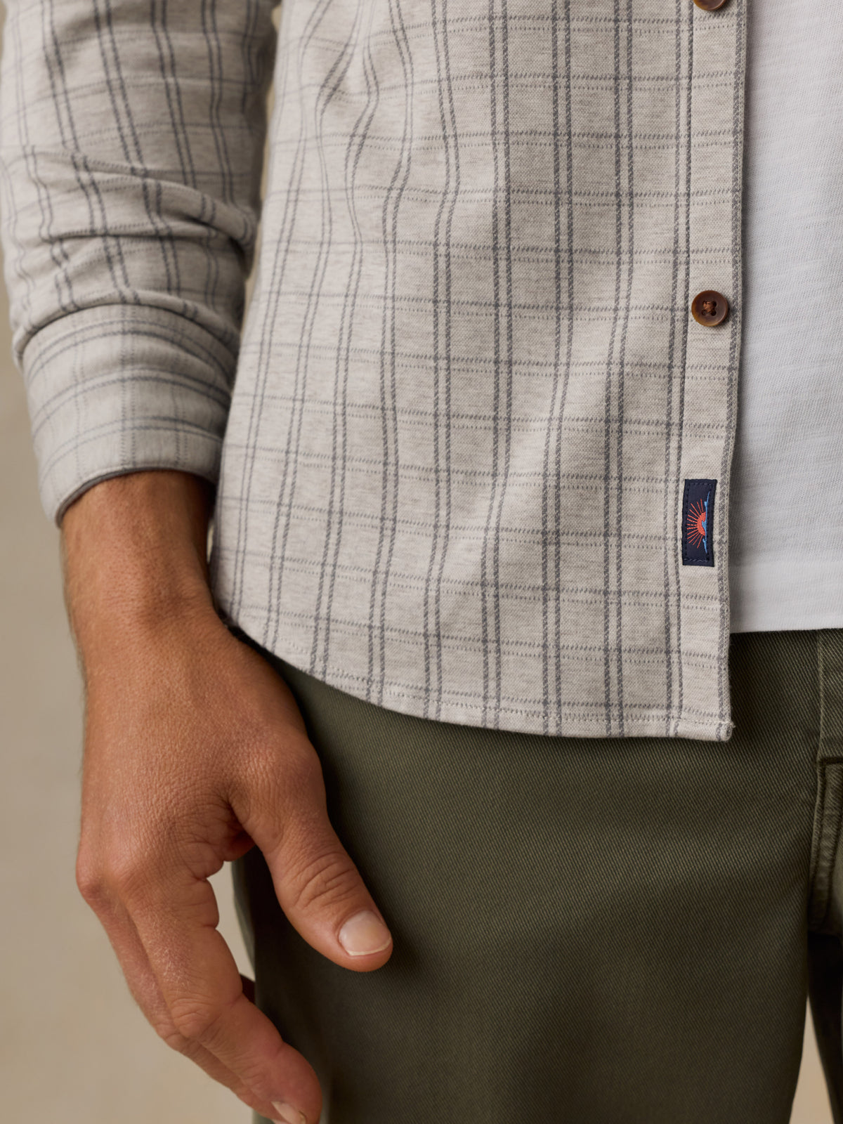 Close-up of a man wearing a light gray and white plaid button-up shirt with brown buttons, paired with olive green trousers., image 4 of 6