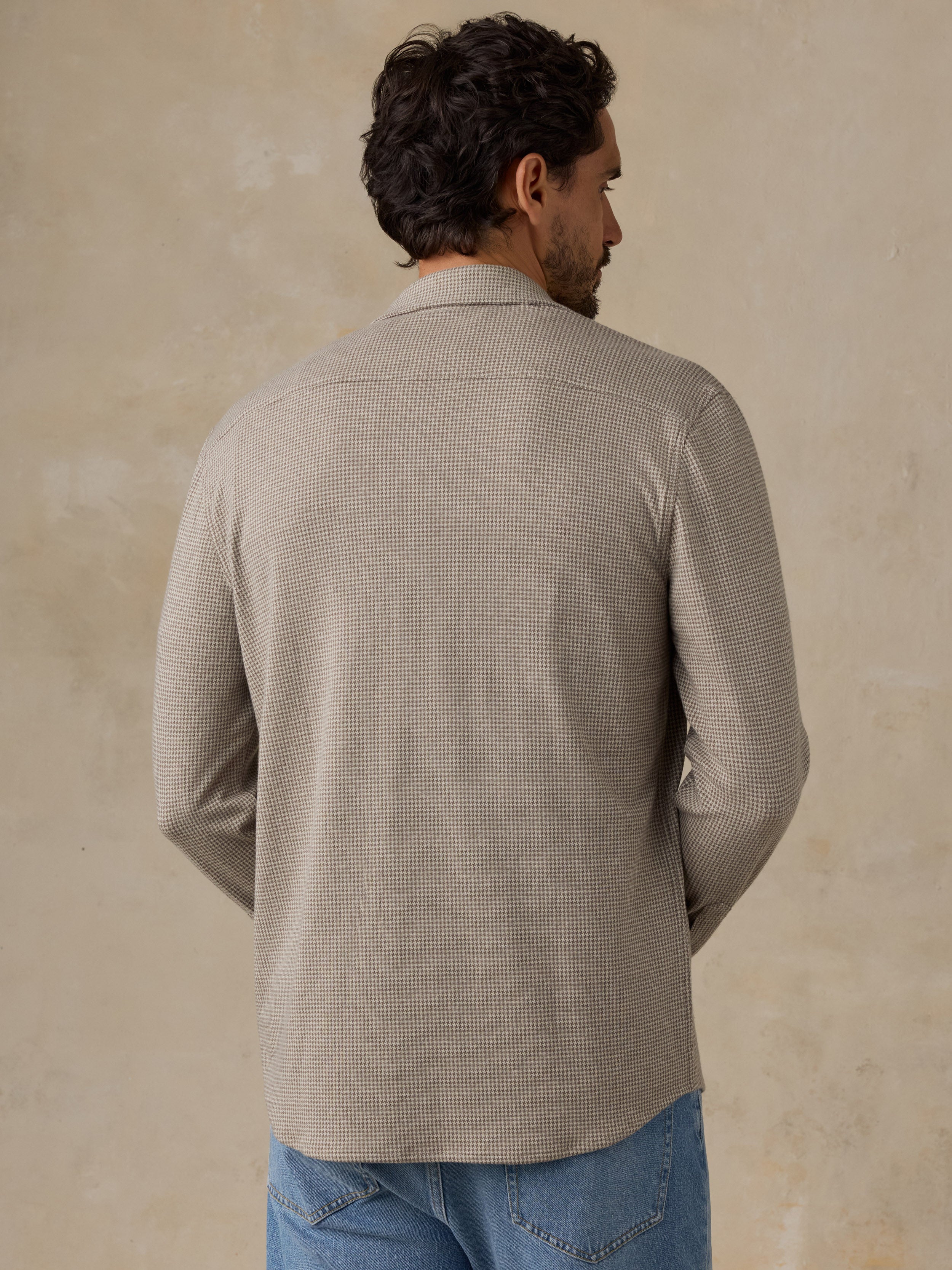 Man wearing a beige overshirt and jeans against a beige studio background