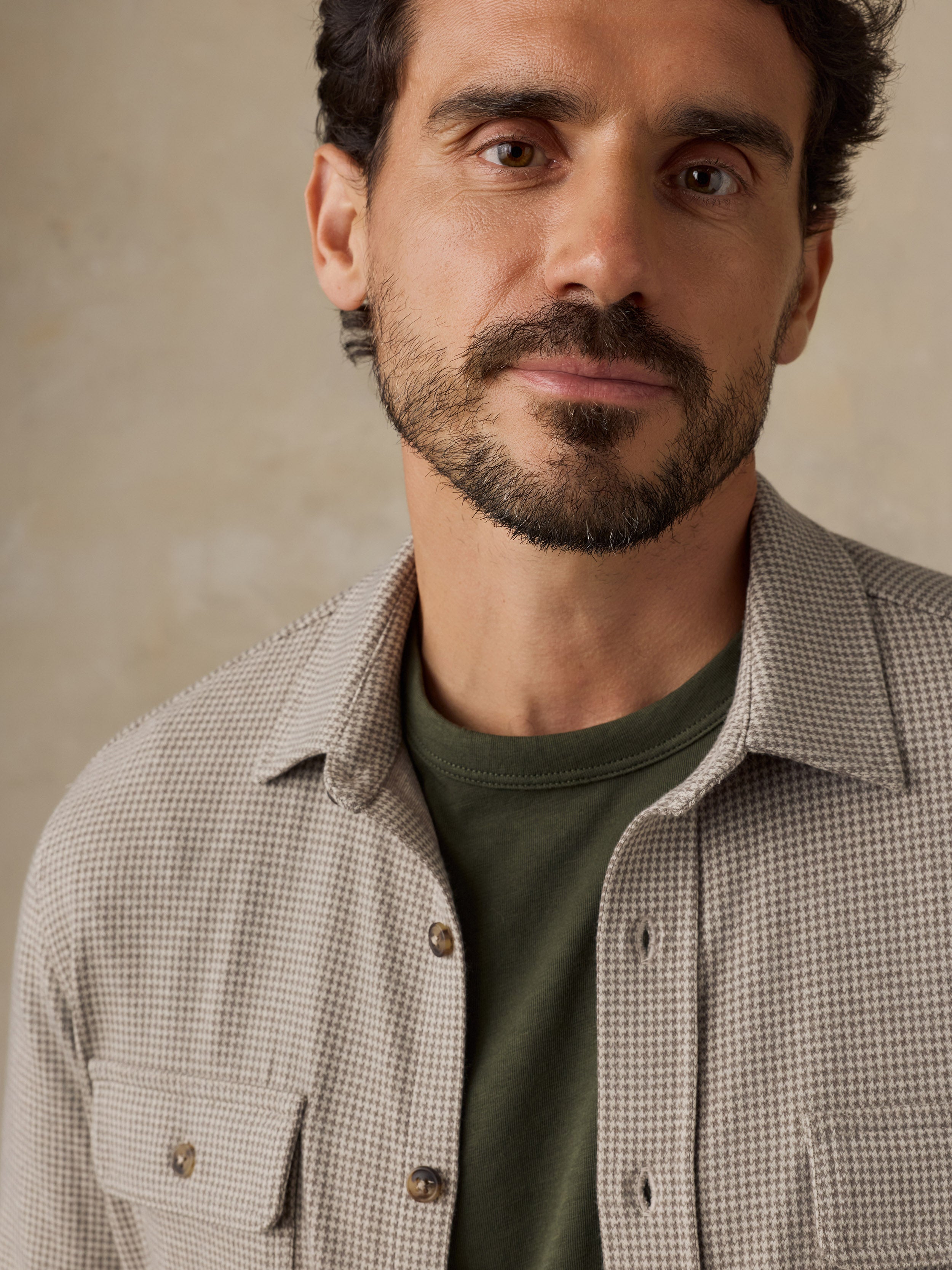 Man wearing a beige overshirt with a green t-shirt against a beige studio background