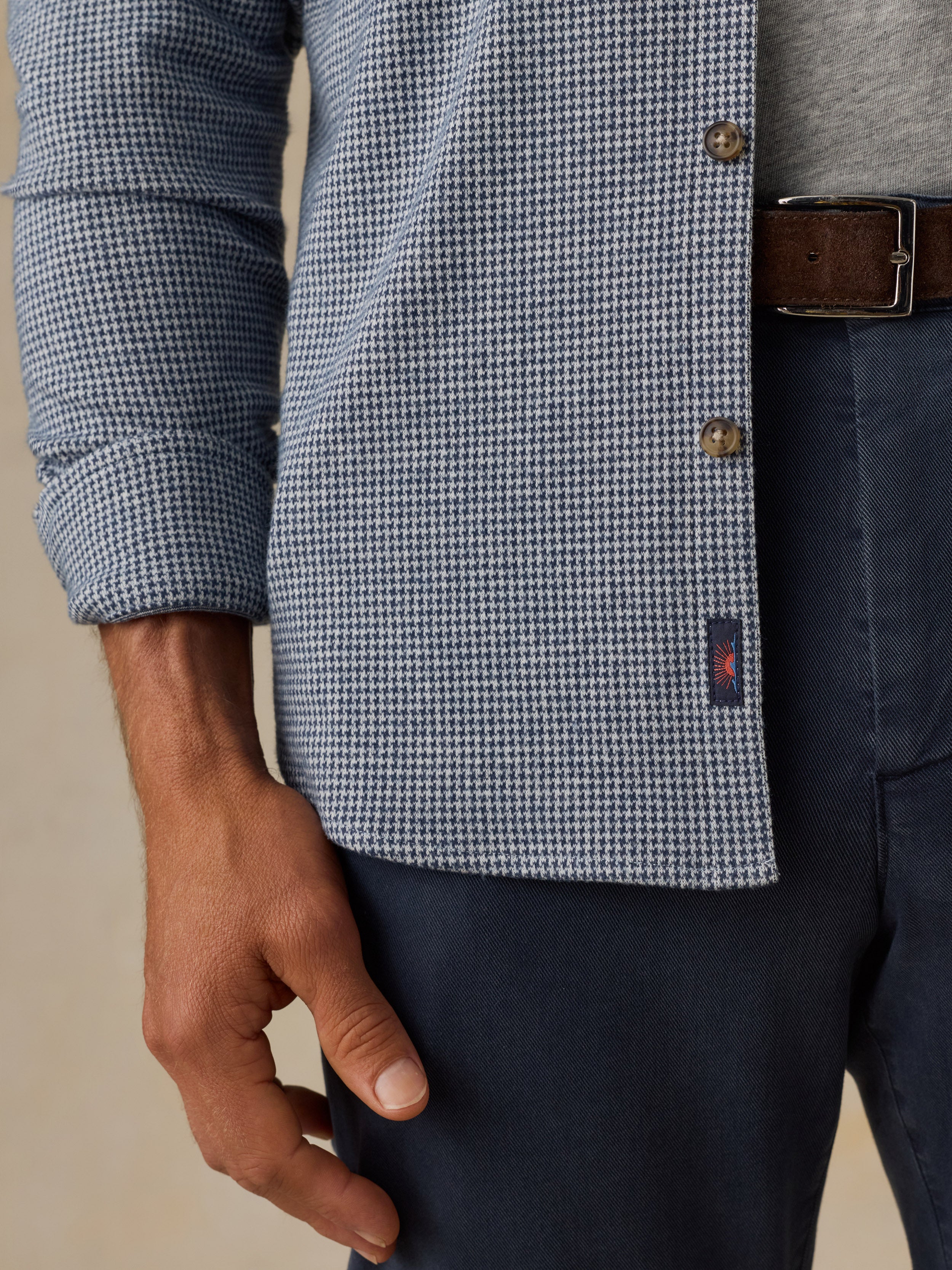 Close-up of a man wearing a blue and white houndstooth patterned button-up shirt, navy trousers, and a brown leather belt.