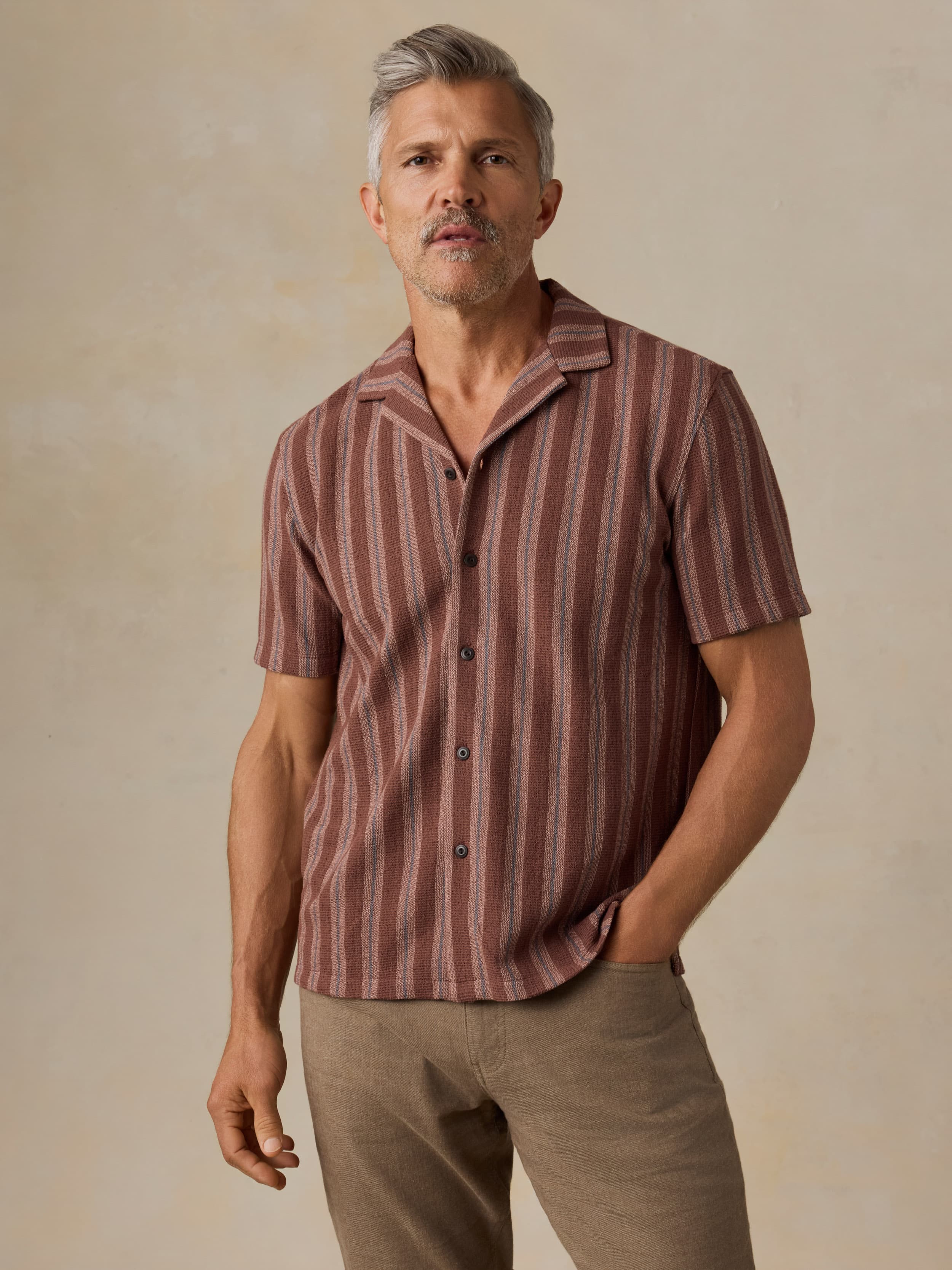 Man wearing a red striped shirt and brown pants against a beige background