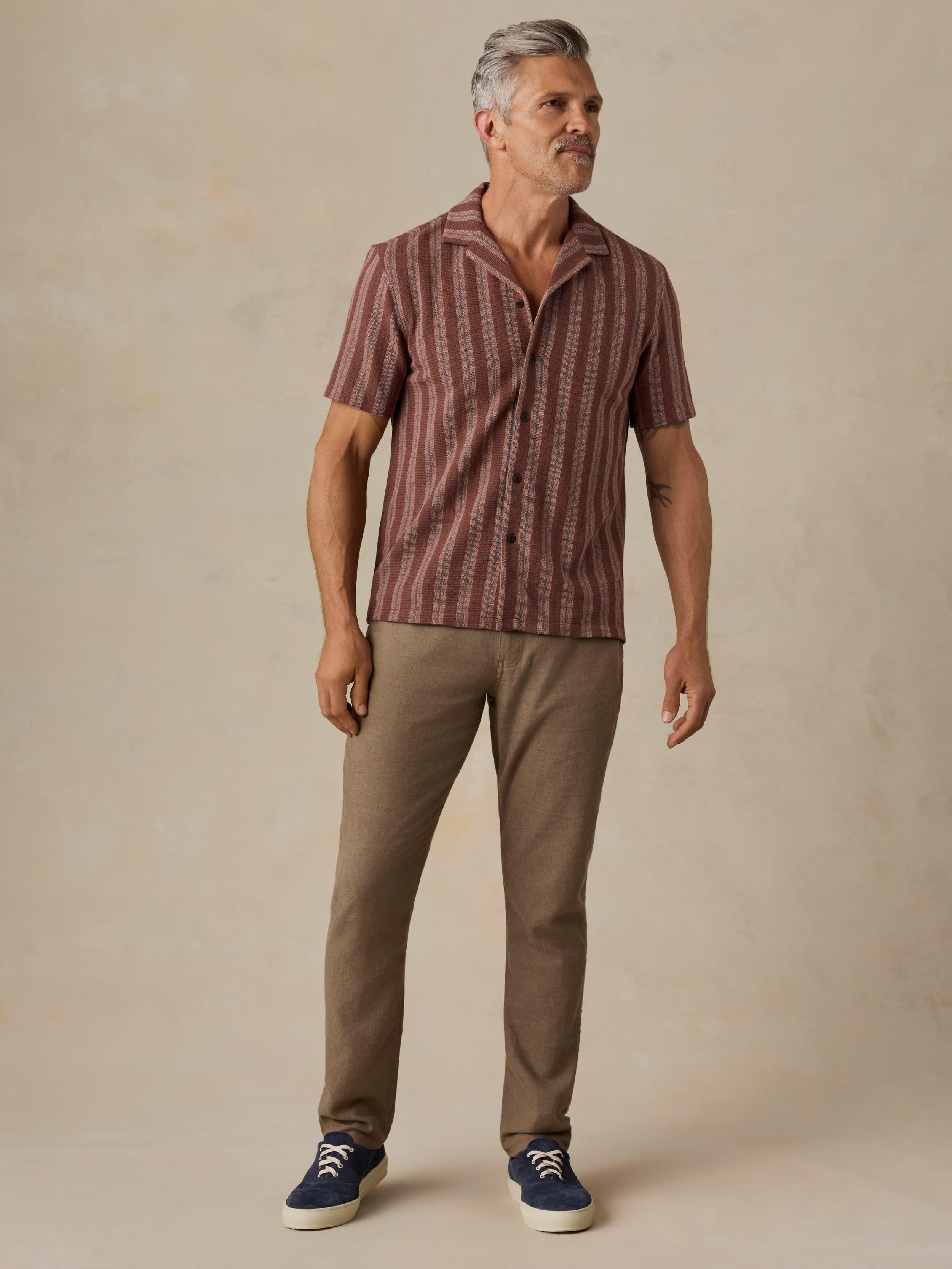 Man wearing a striped shirt and brown pants against a beige background