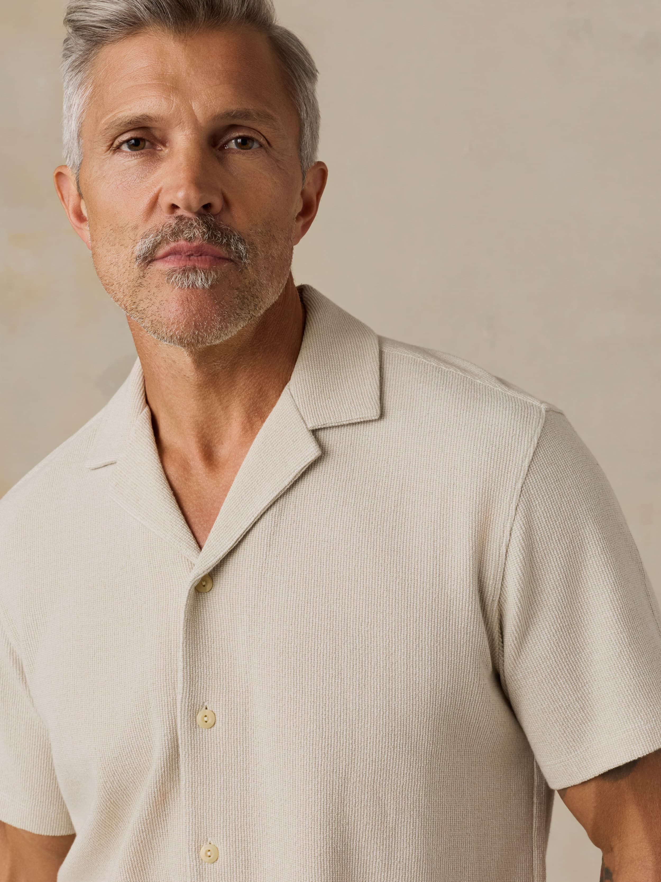 Man wearing a beige short-sleeve shirt against a neutral background