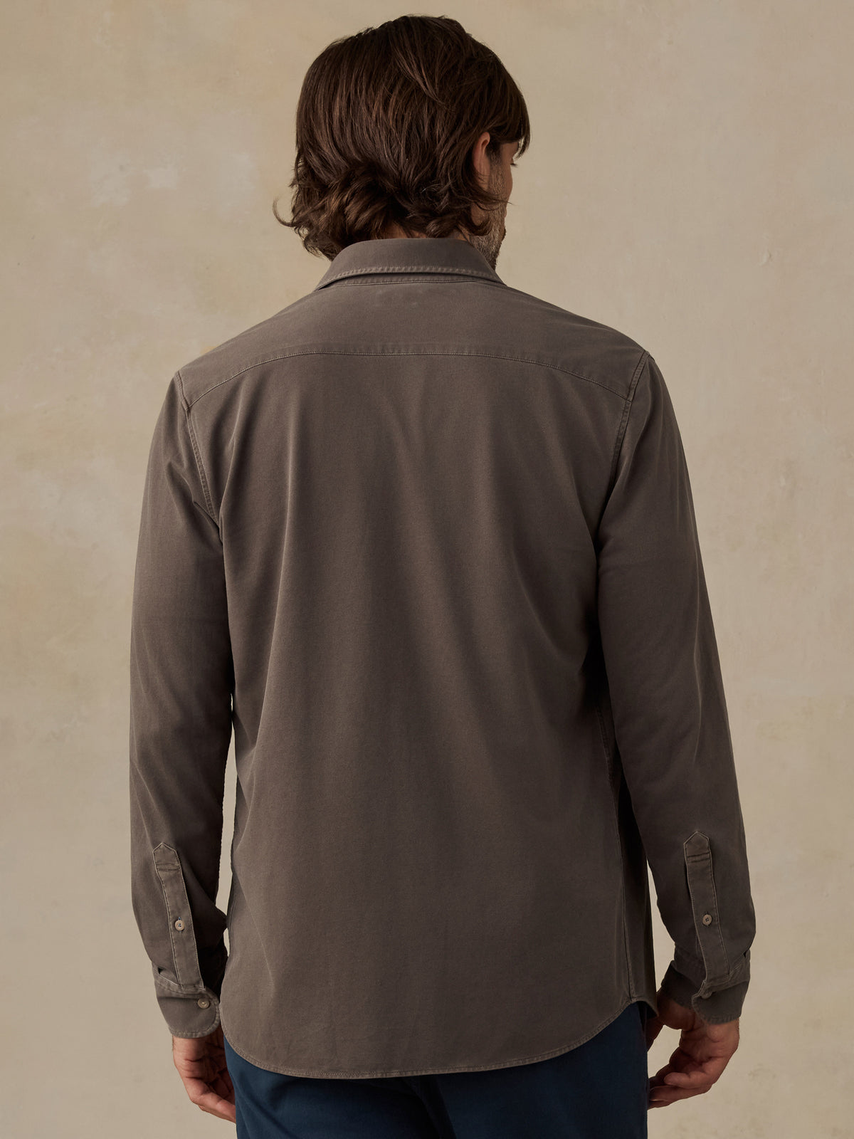 Man wearing a brown button down shirt and navy chino pants against a beige background, image 3 of 5