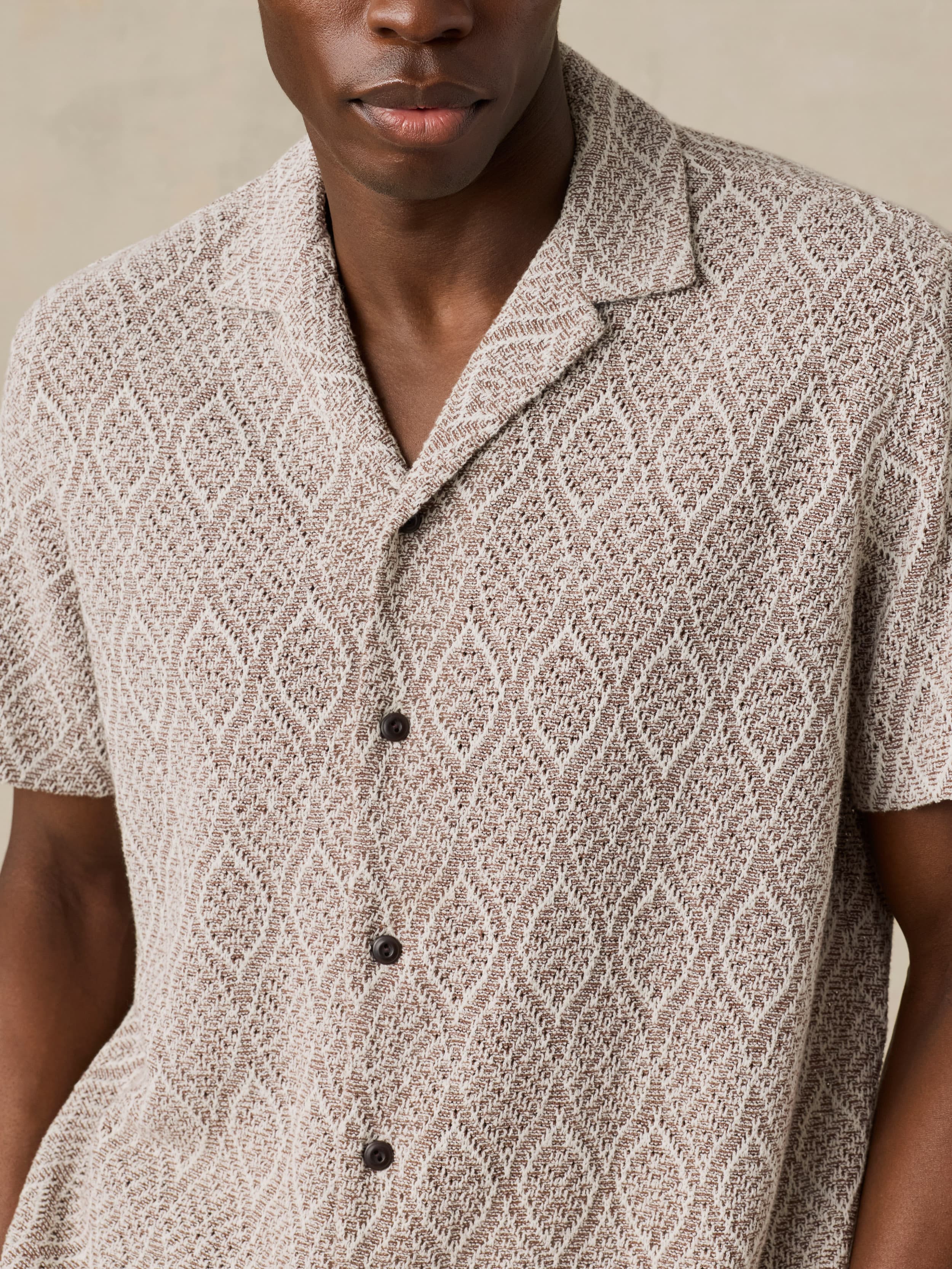 Man wearing a brown patterned shirt with a neutral background