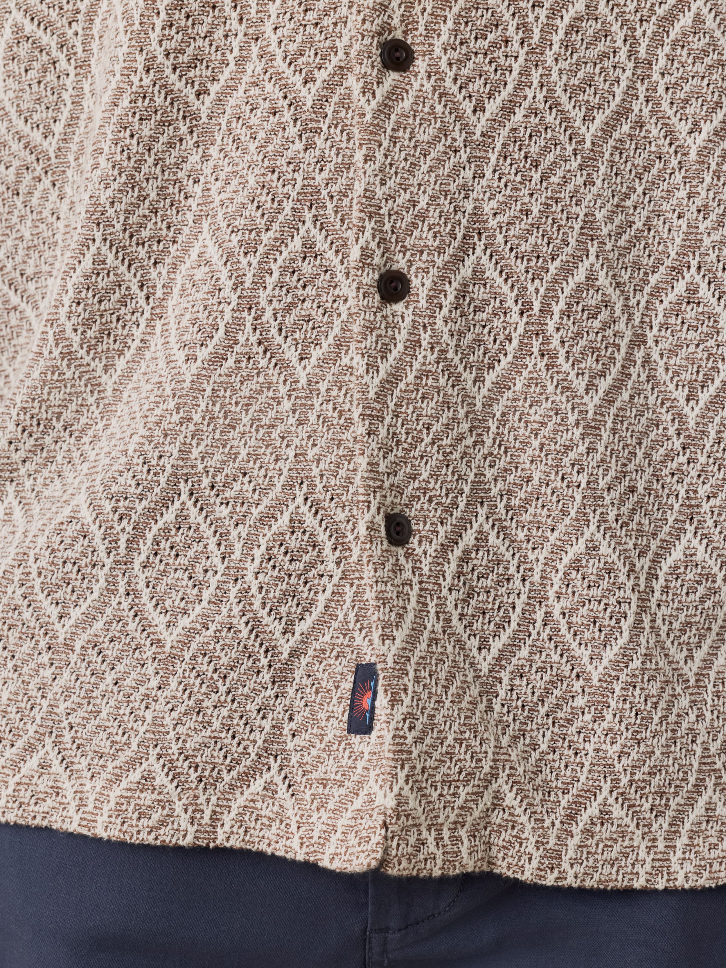 Close-up of a textured brown shirt with black buttons and a Faherty brand label.