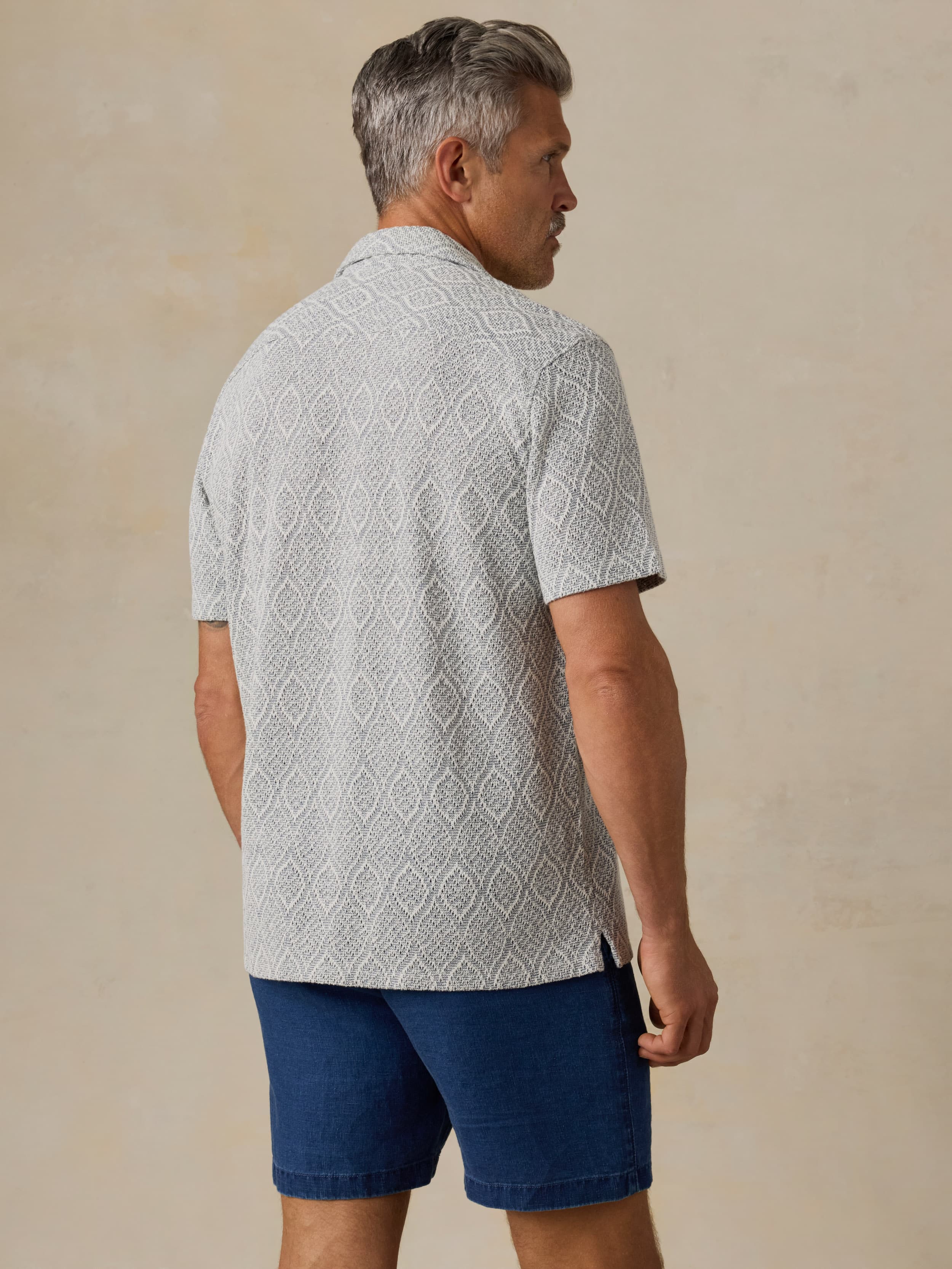 Man wearing a patterned light blue shirt and blue shorts against a beige background