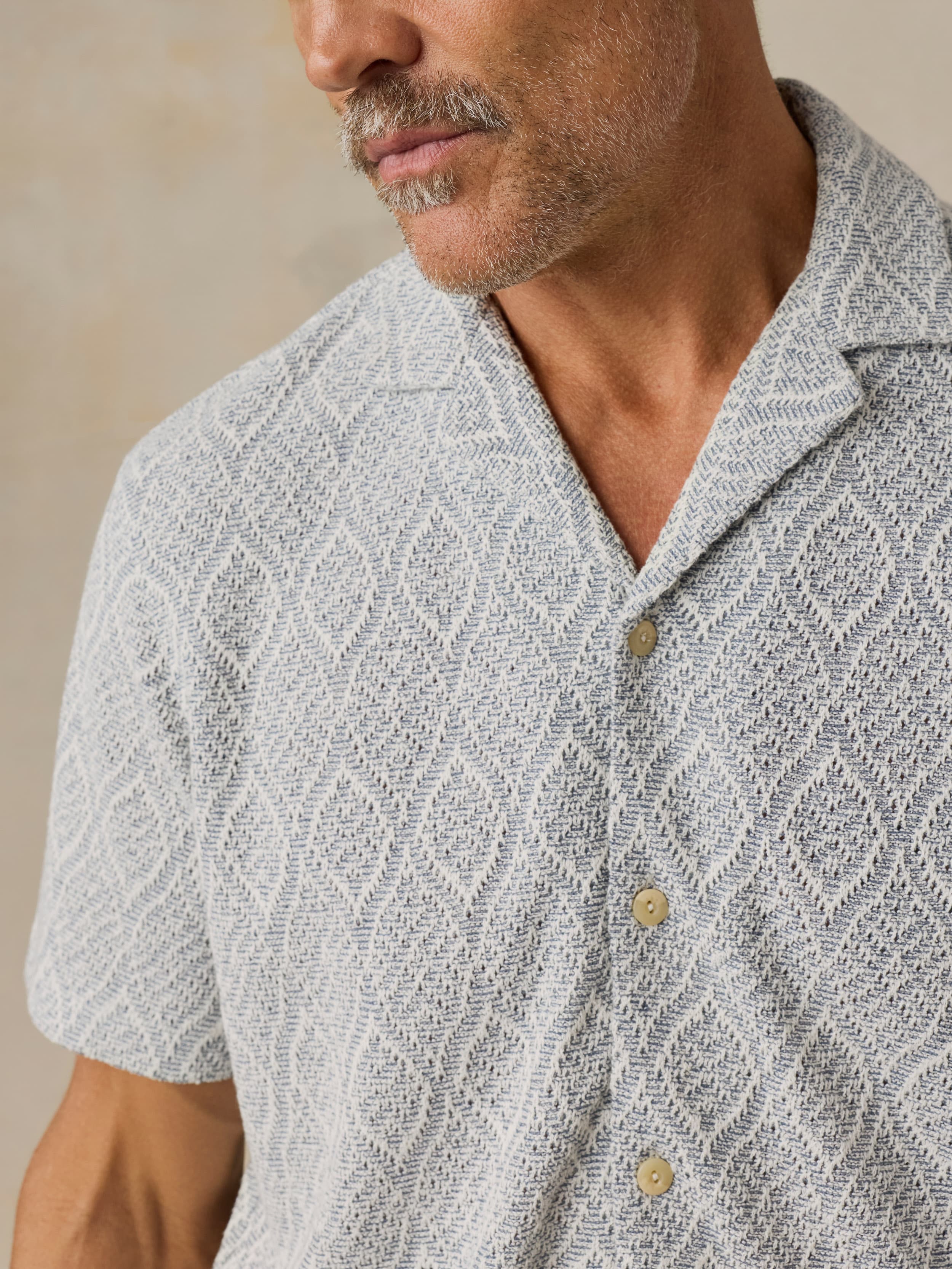 Man wearing a patterned light blue shirt against a beige background