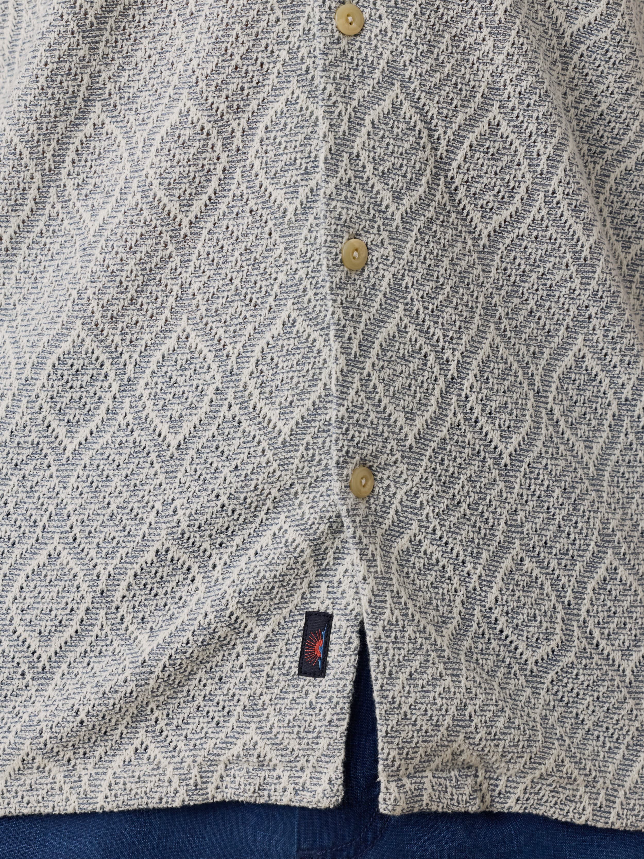 Close-up of a textured light blue shirt with button details and a Faherty brand tag.