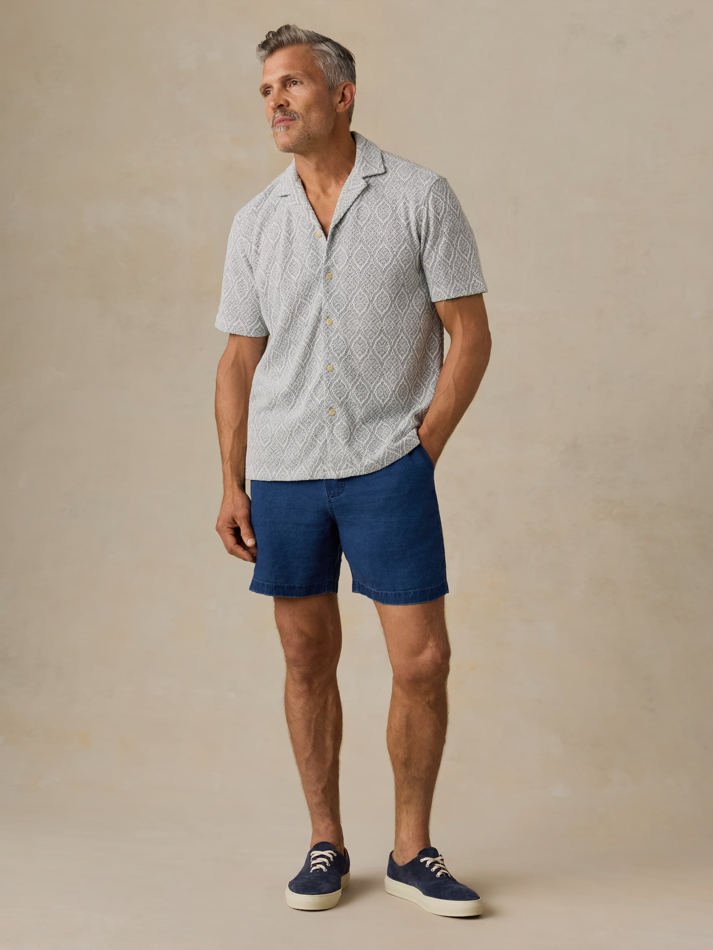 Man wearing a patterned light blue shirt and blue shorts against a beige background