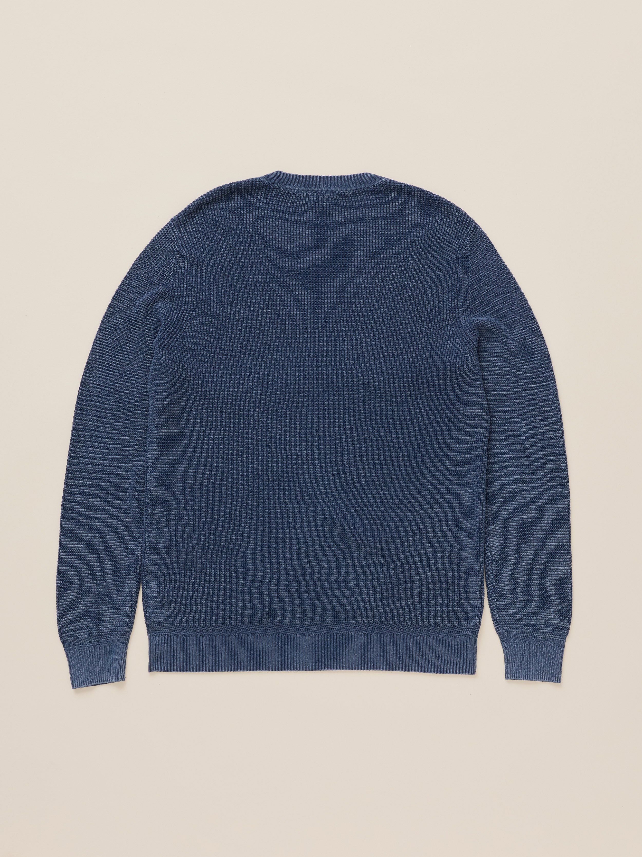 A dark blue ribbed knit sweater shown from the back, laid flat against a light beige background.